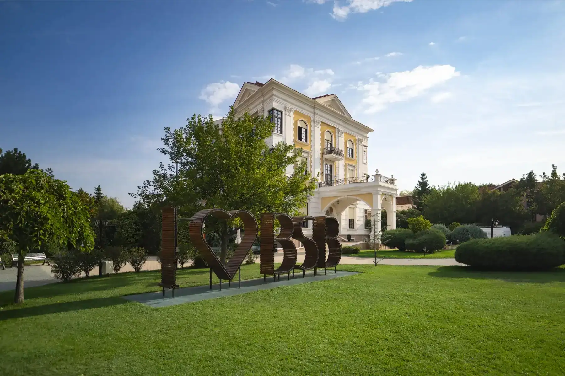 A lush green lawn with a decorative "I ❤️ BSB" sign in front of a grand, historic building under a b.