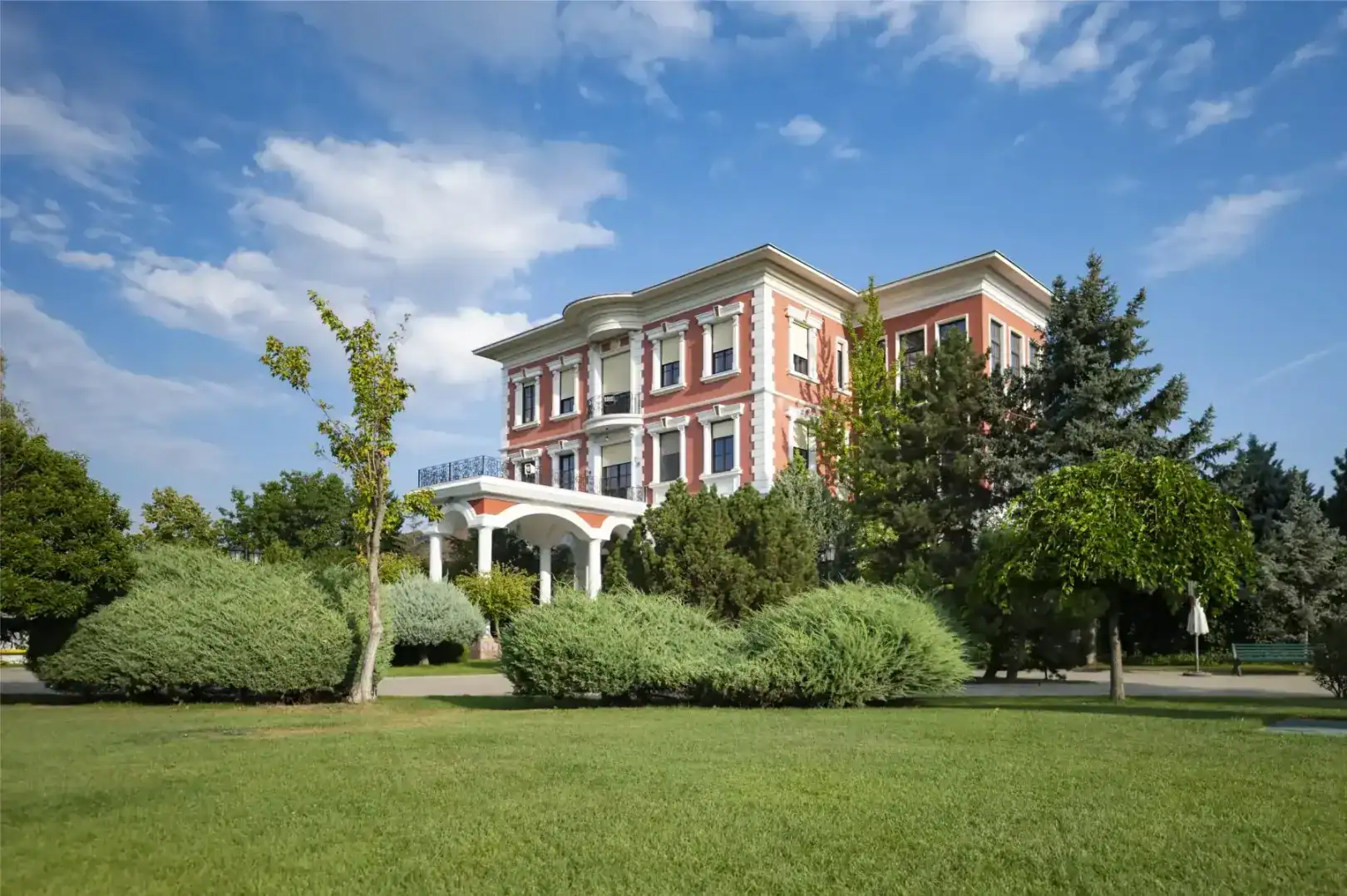 A lush green park with a historic pink and white mansion under a blue sky.