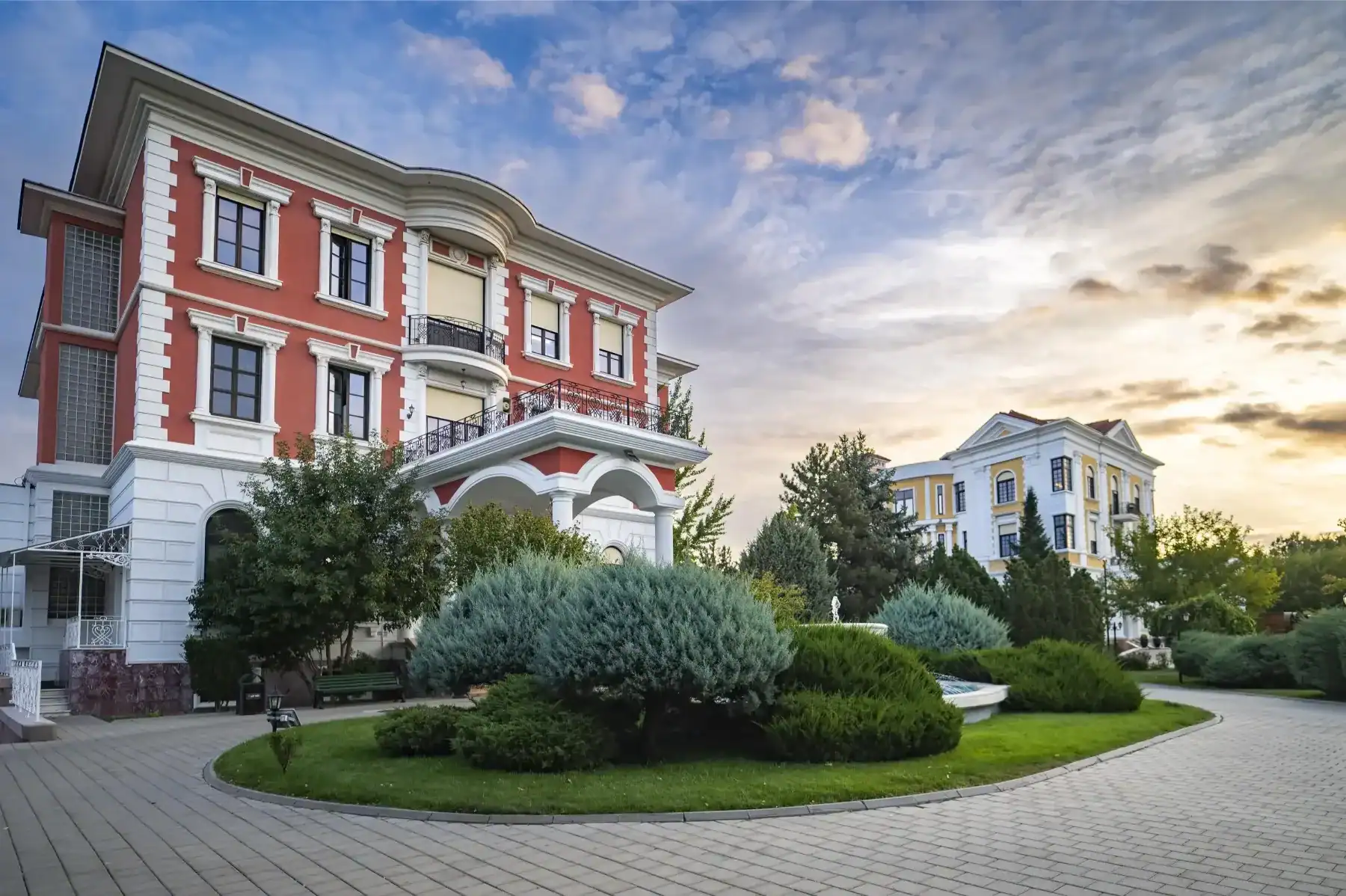 Elegant European-style school building with lush greenery and a scenic sky backdrop.