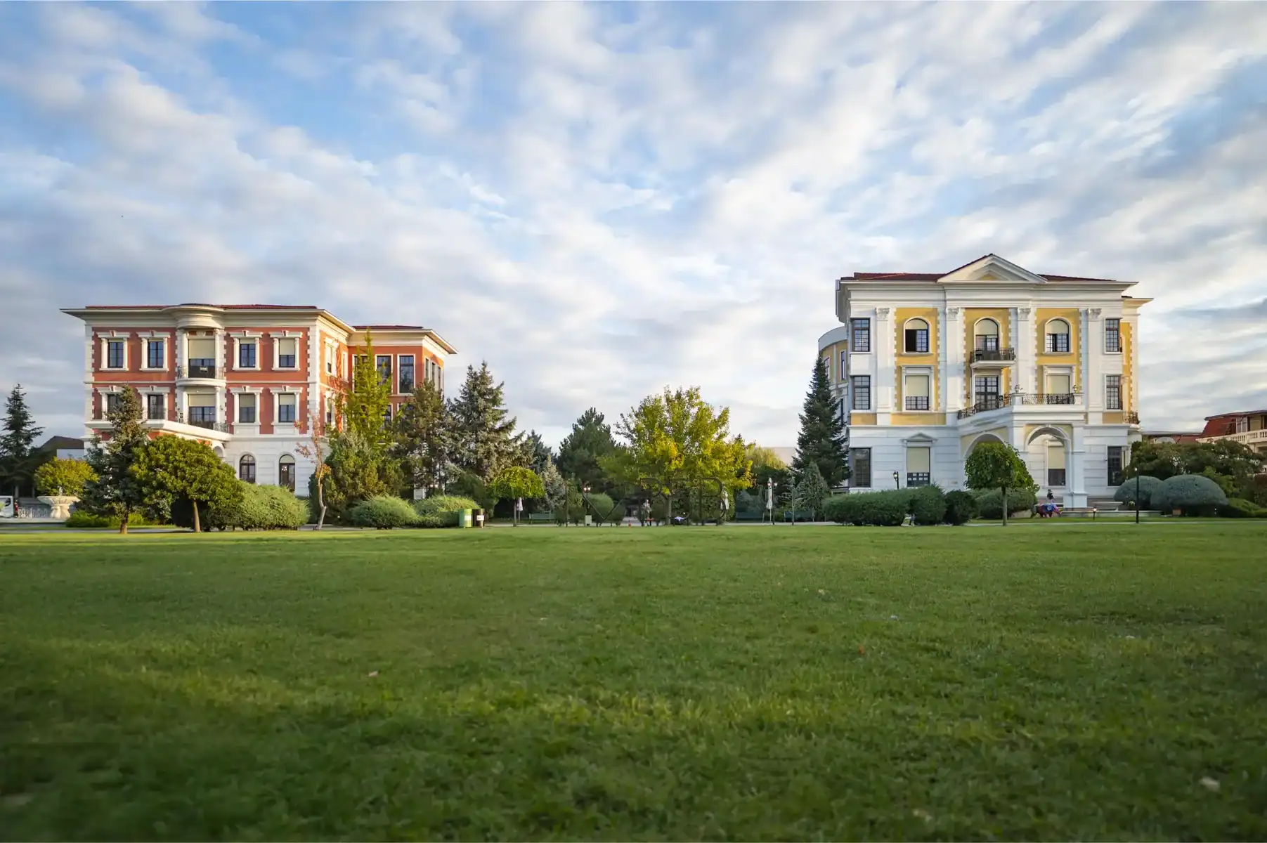 Modern luxury residential buildings with lush green lawns and clear sky in the background.