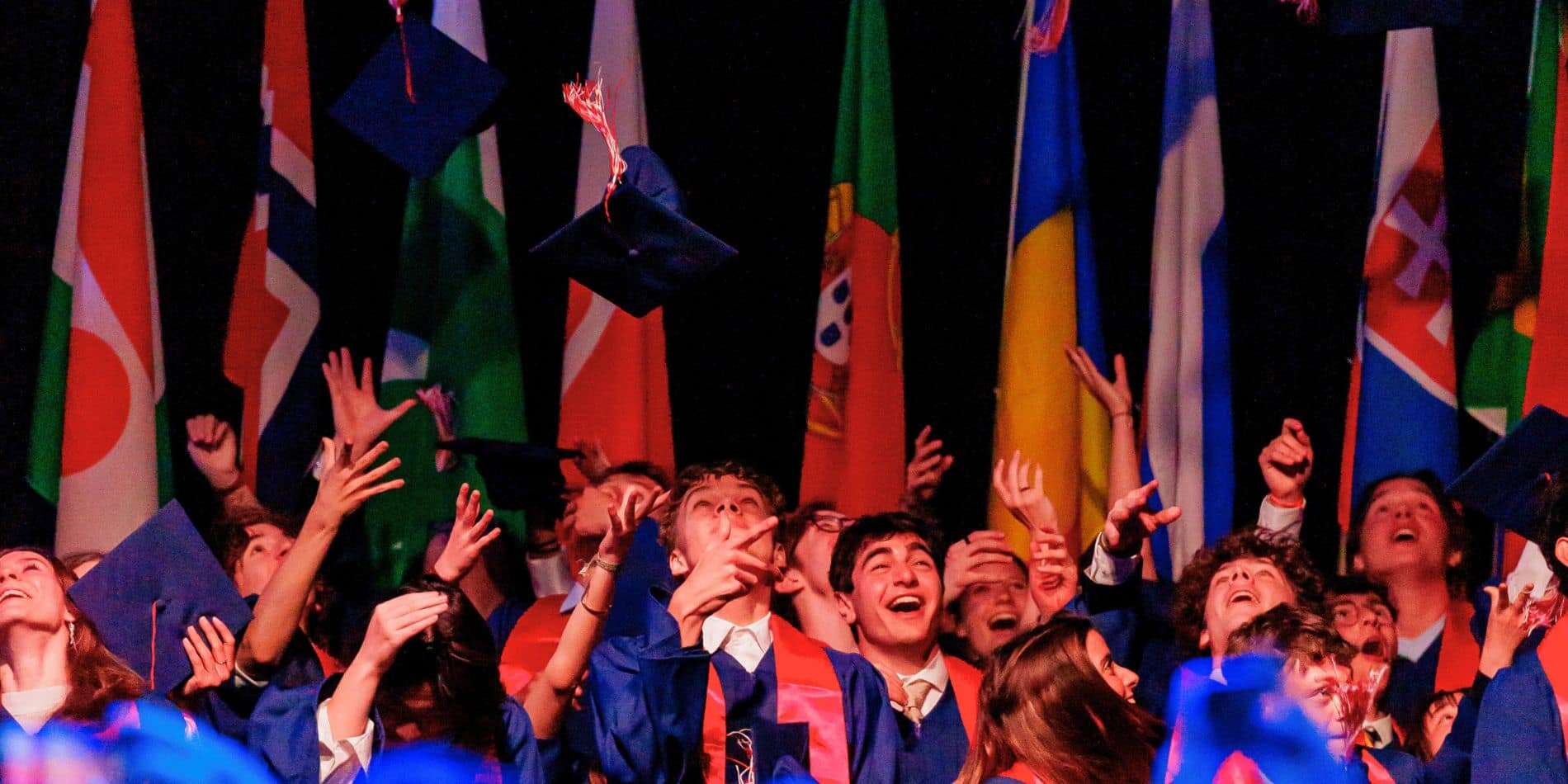Graduates celebrating at the International School of Brussels with diplomas and caps in front of int.