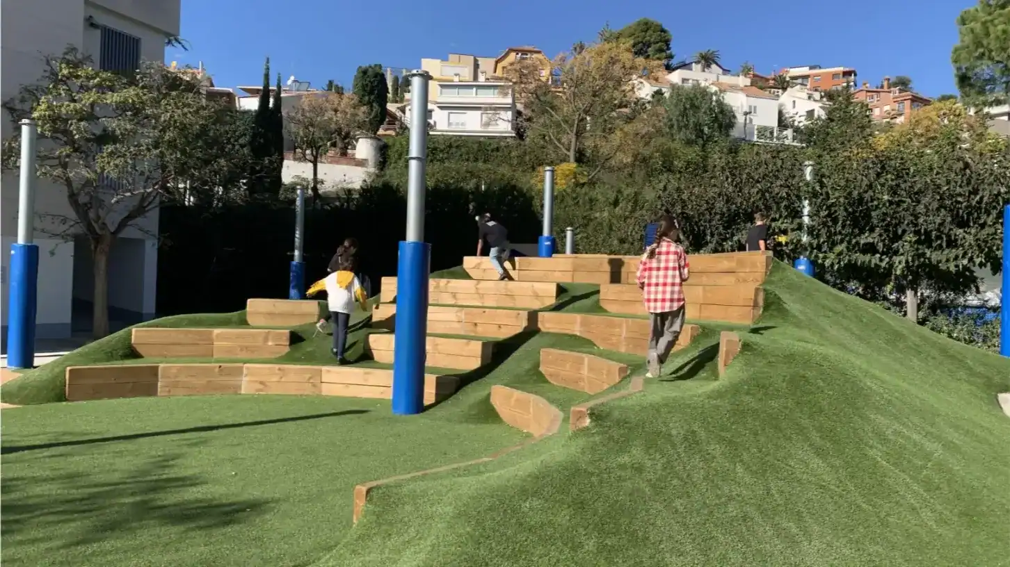 Outdoor playground with wooden steps and green turf at American School of Barcelona.