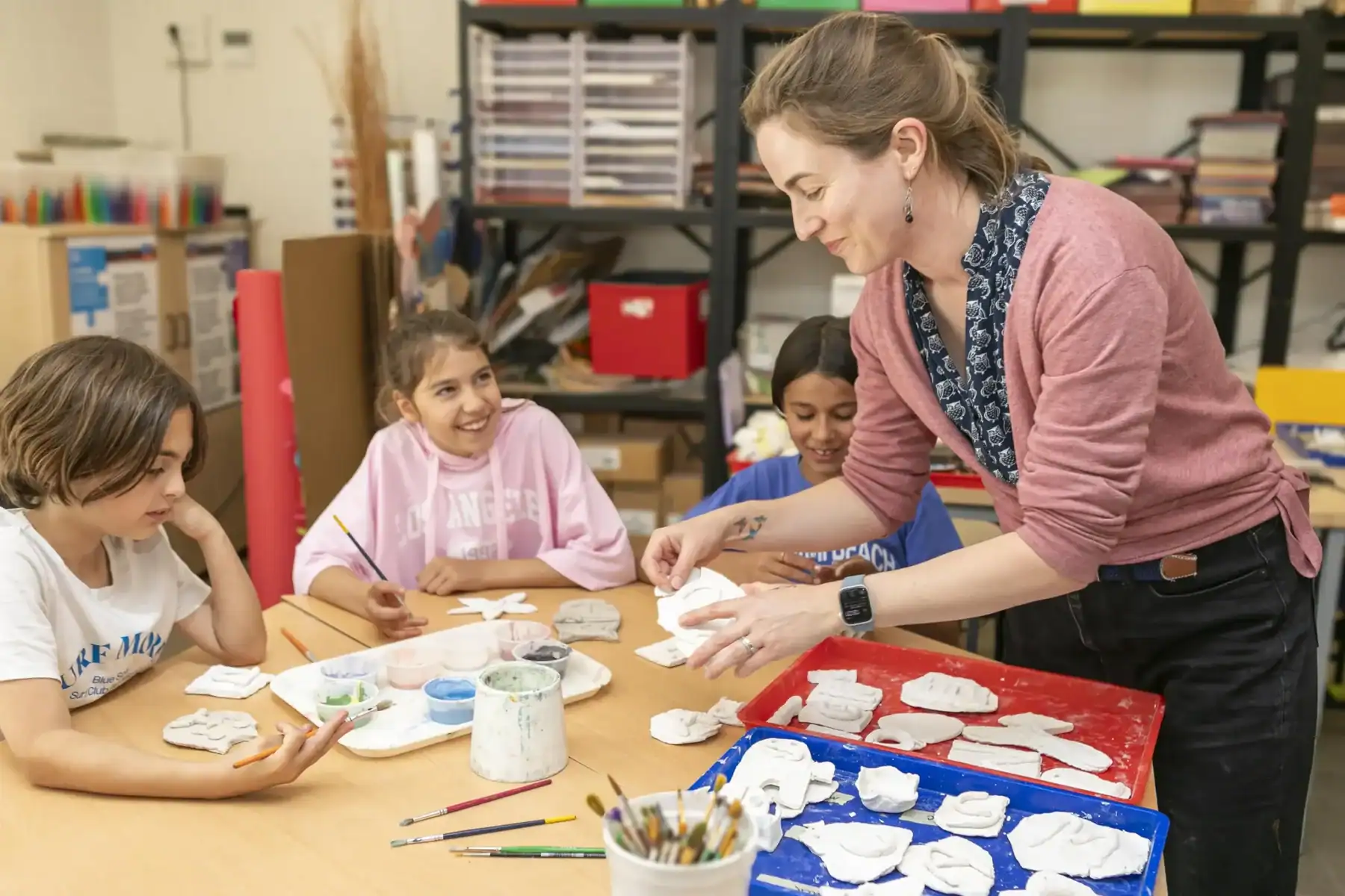 Art teacher assisting students with clay sculpture projects in classroom setting.