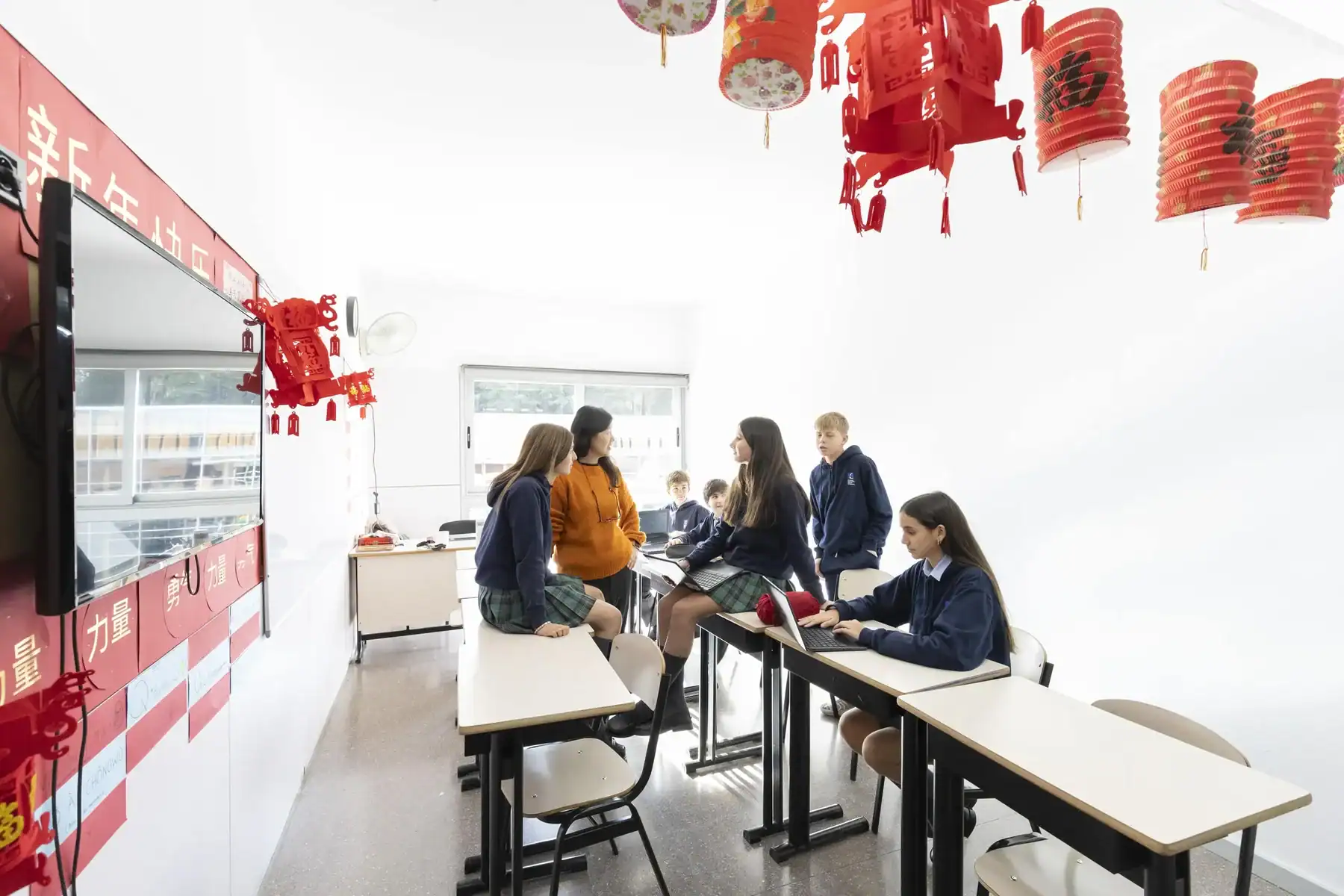 Group of students in a bright classroom with red lanterns and a large screen.