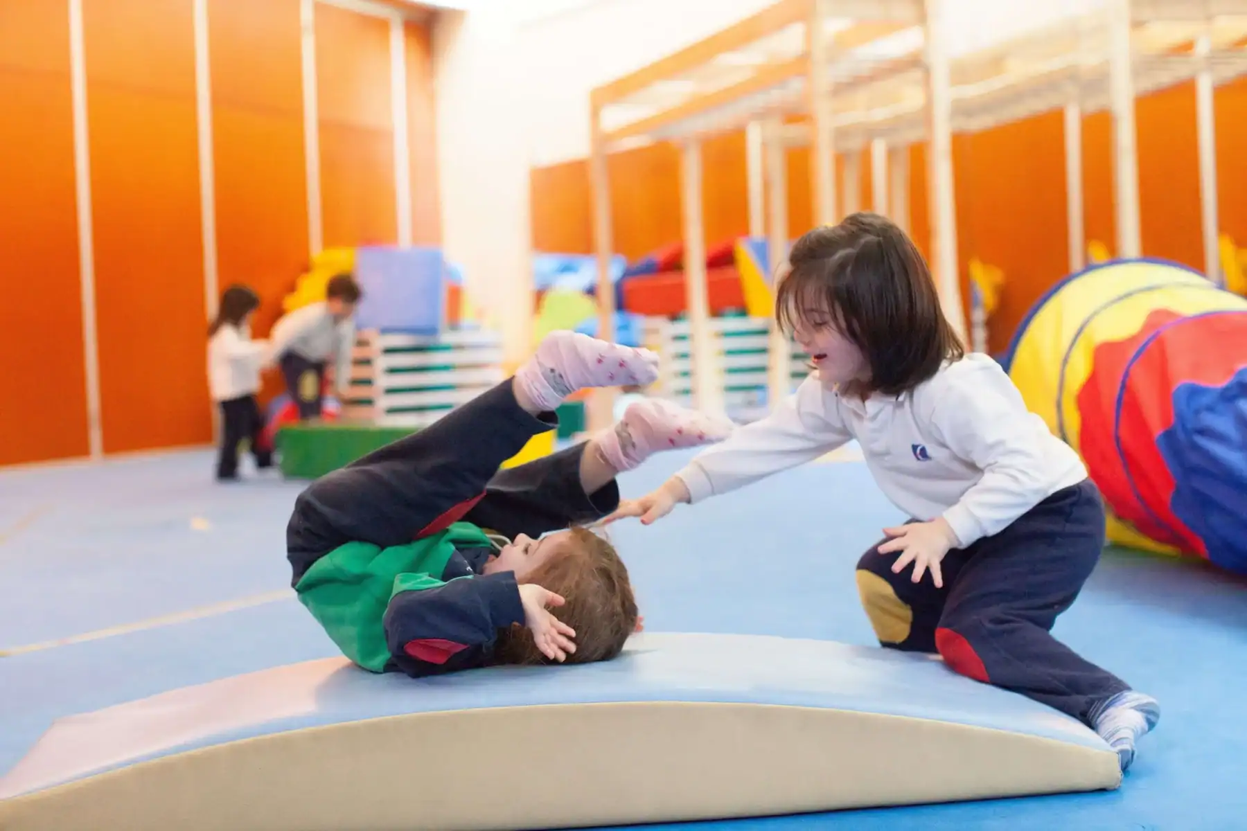 Children playing on soft gym mats in a colorful indoor play area.