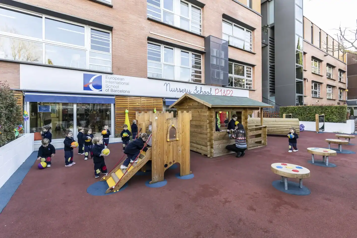 European International School of Barcelona playground with wooden play structure and students.