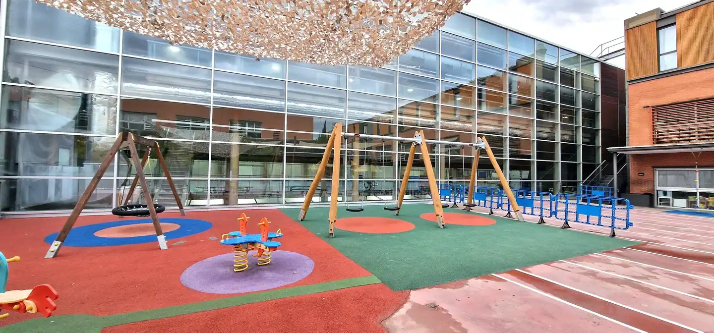 Playground at European International School of Barcelona with swings and colorful safety flooring.