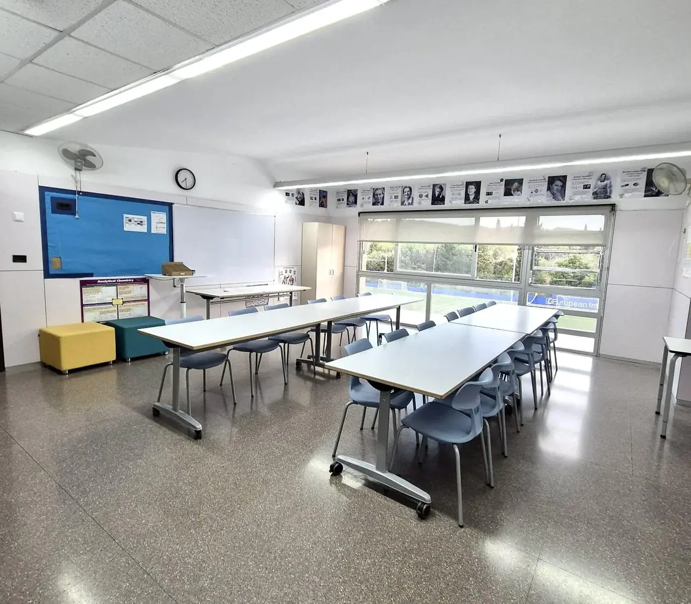 Bright classroom with long white tables and blue chairs in a modern school setting.