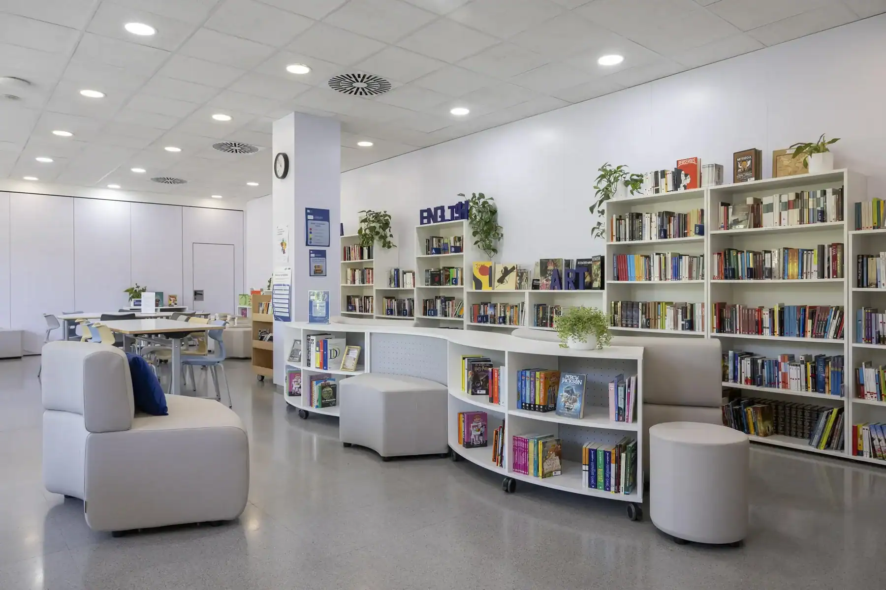 Modern library interior with white shelves, plants, and seating.