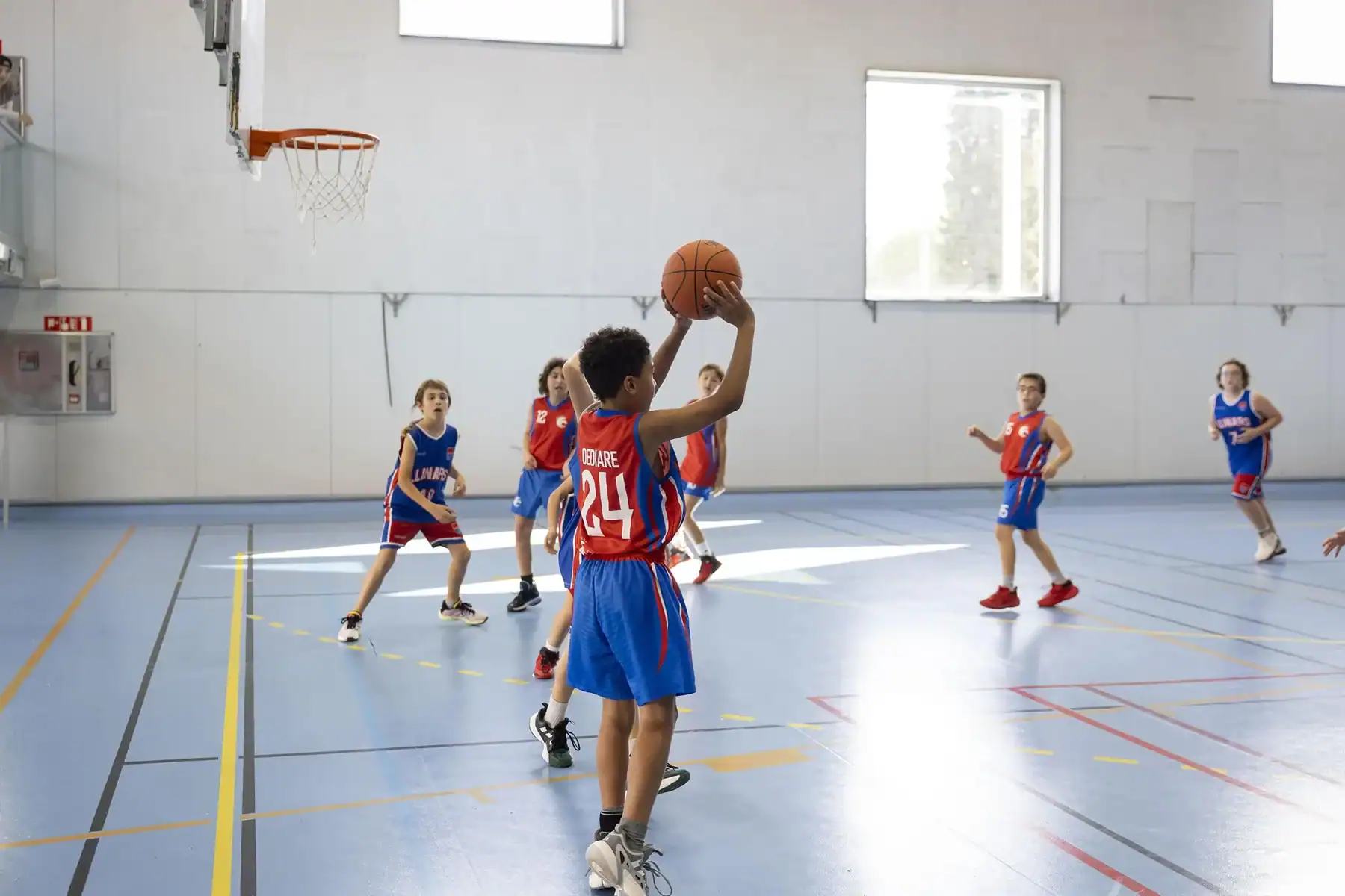Basketball player in blue and red jersey shooting near basketball hoop in a gymnasium.