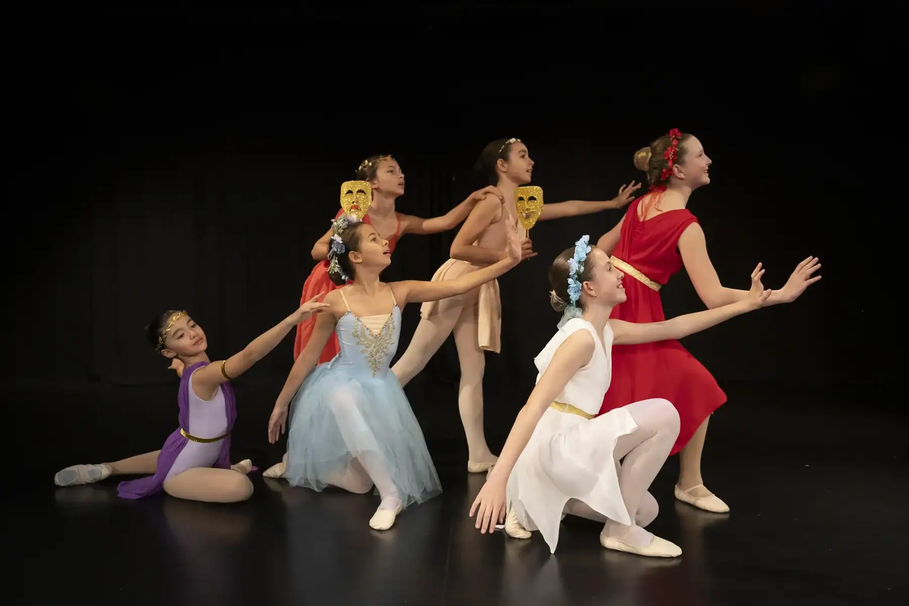 Group of ballet dancers on stage with masks performing a routine.