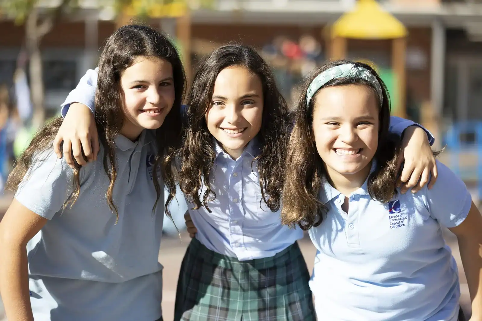 Three smiling schoolgirls with arms around each other in a schoolyard.