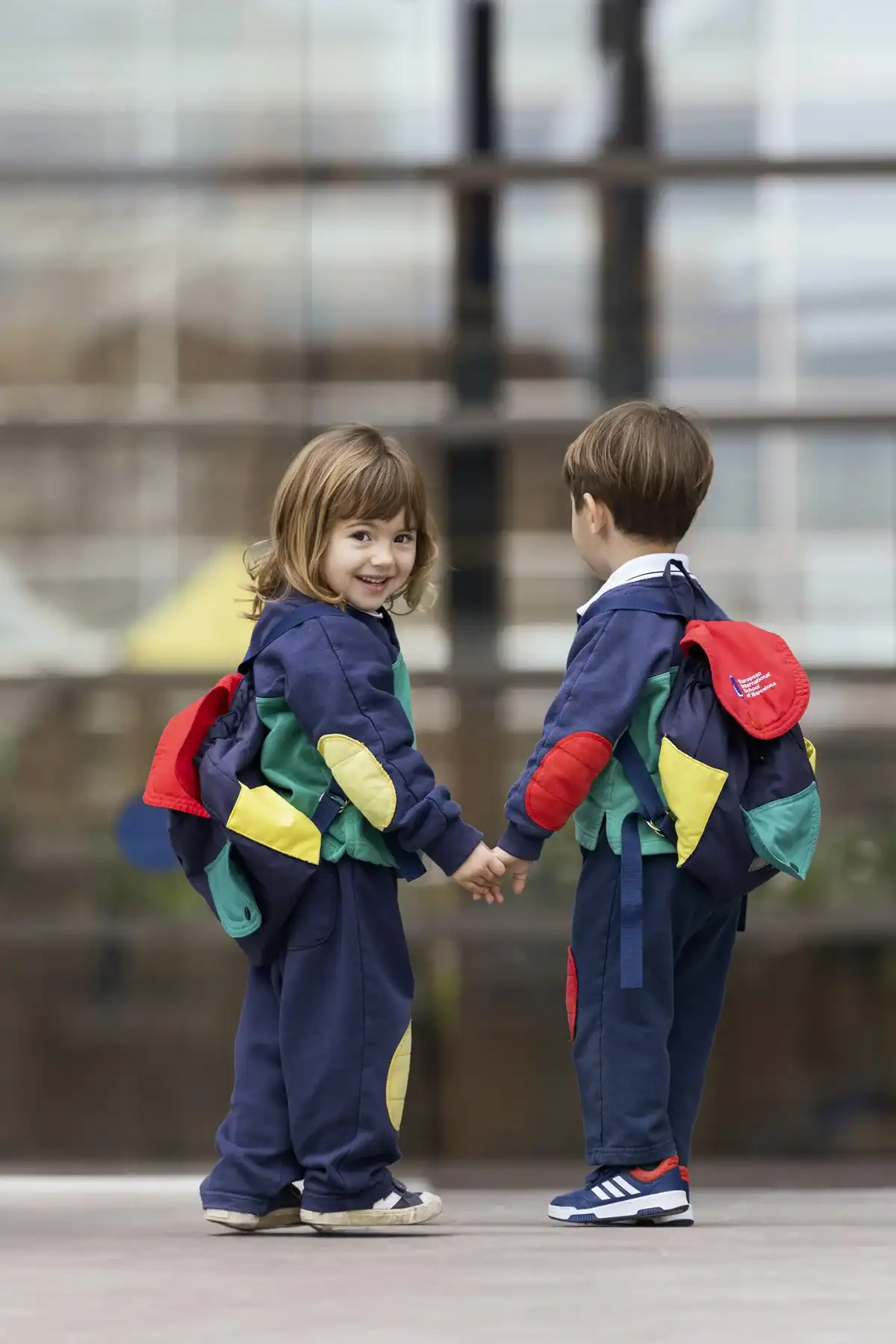 Two young children in matching blue outfits holding hands outside.