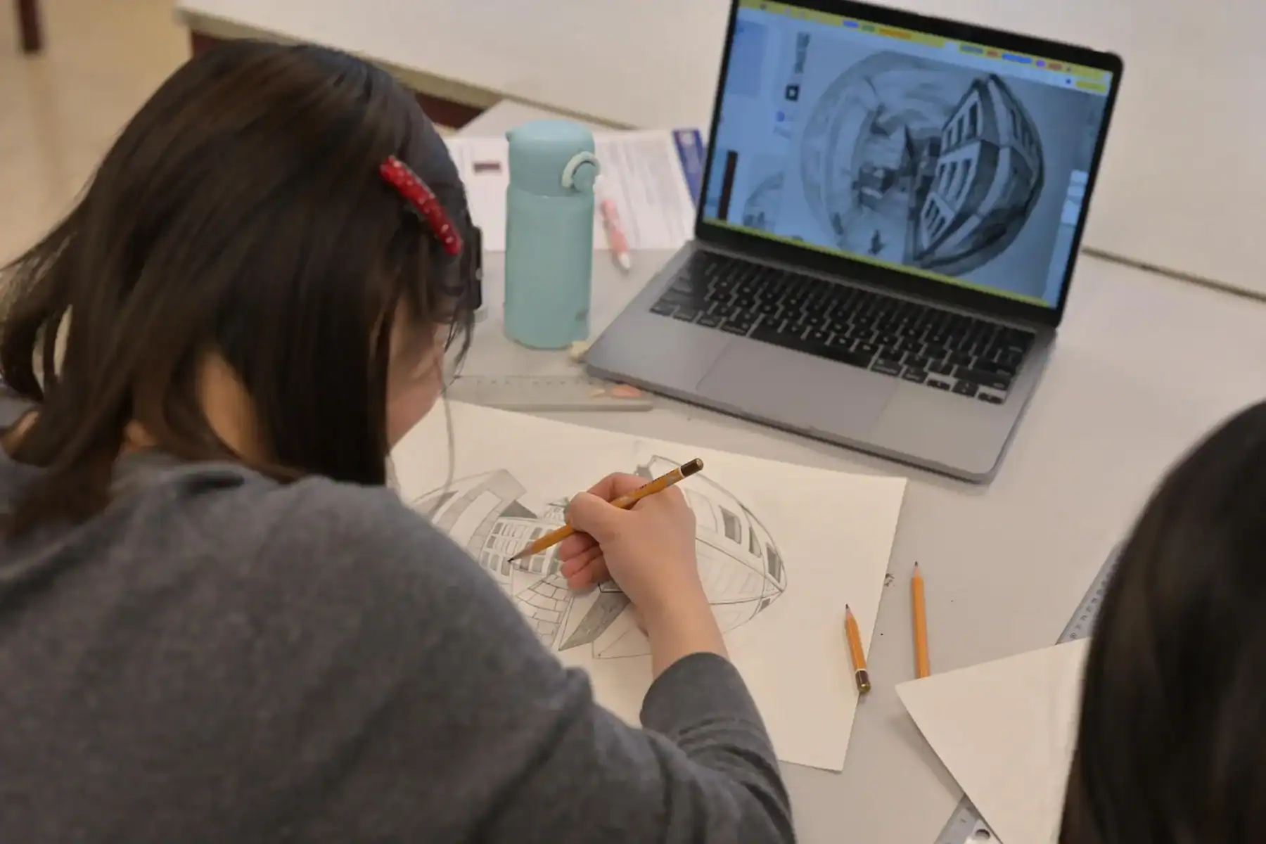 Student working on architectural design with laptop and sketches at International School of Brussels.