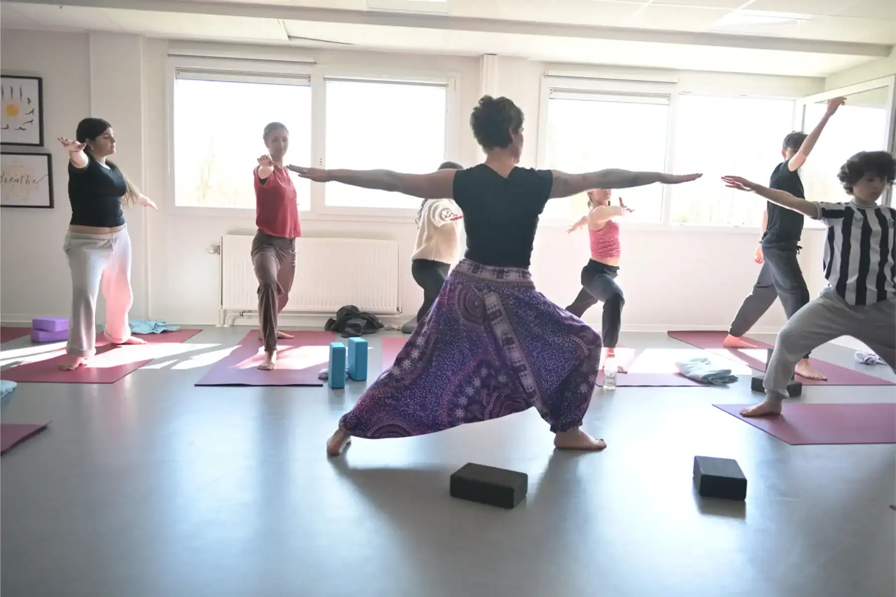 Yoga class with students practicing poses in a bright classroom.