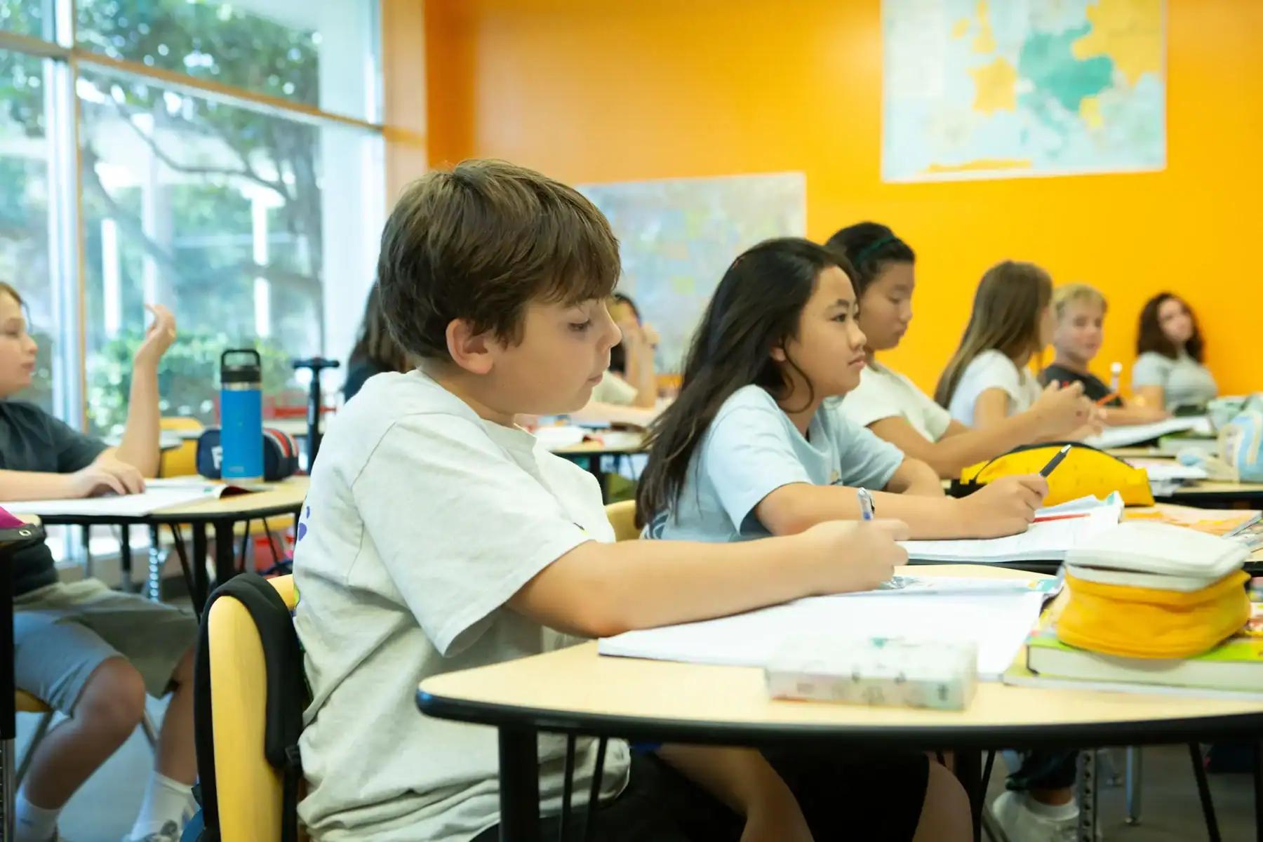 Students attentively learning in a bright classroom with yellow walls.