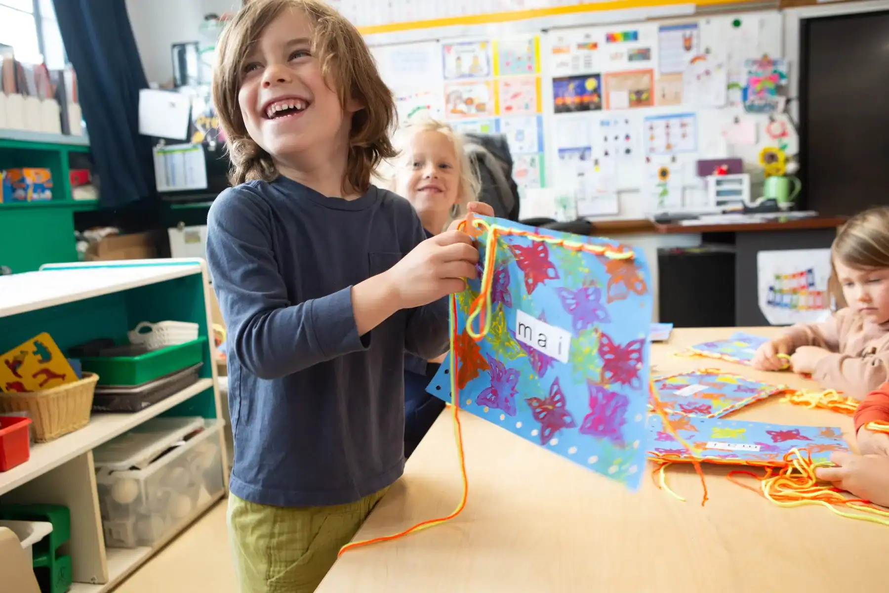 Child smiling while holding a colorful handmade artwork at school.