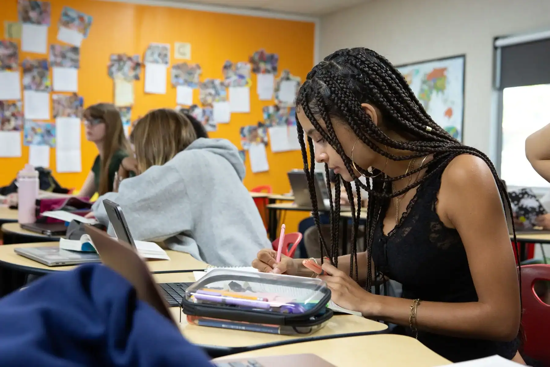 Student in a classroom writing with a pencil and tablet in view.