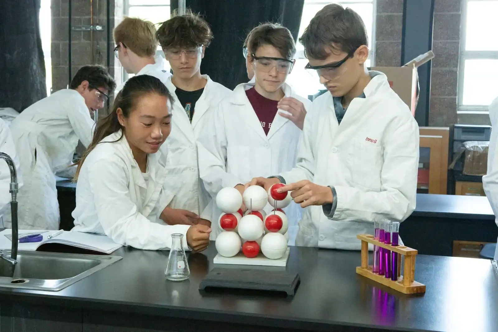 Students in lab coats conducting a chemistry experiment with molecular model in a classroom.
