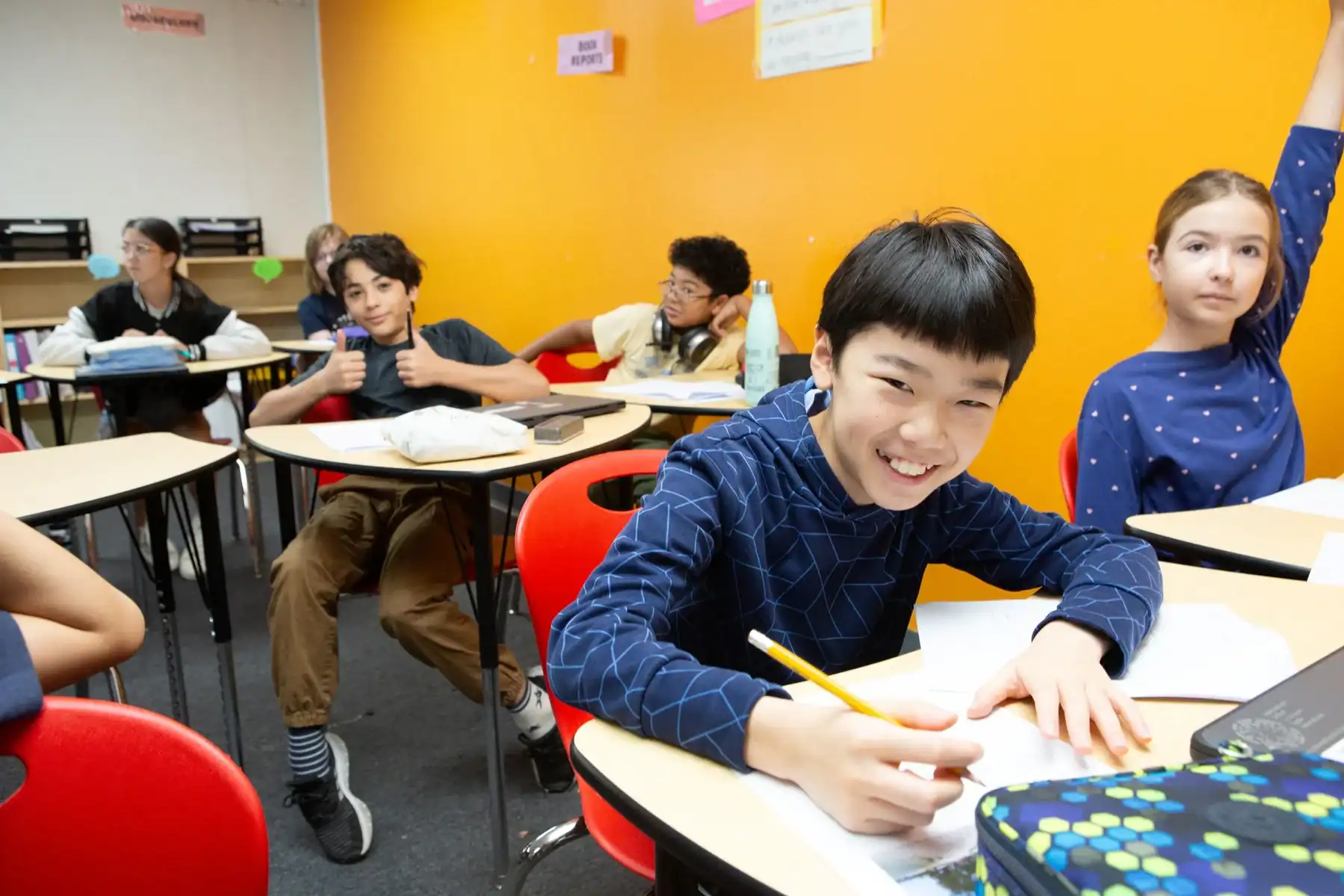 Group of students in a bright classroom collaborating and writing at their desks.