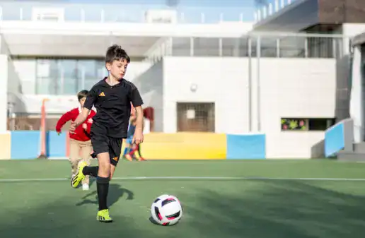 Children playing soccer on a modern school sports field in Madrid.