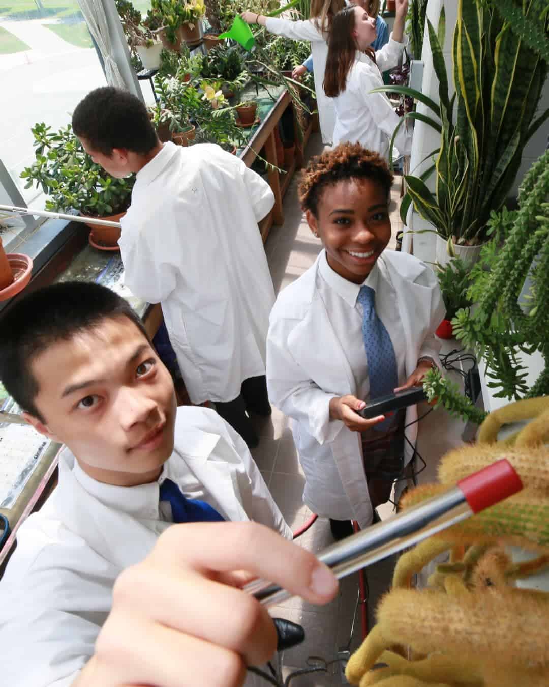 Students in white lab coats working with plants in a greenhouse.