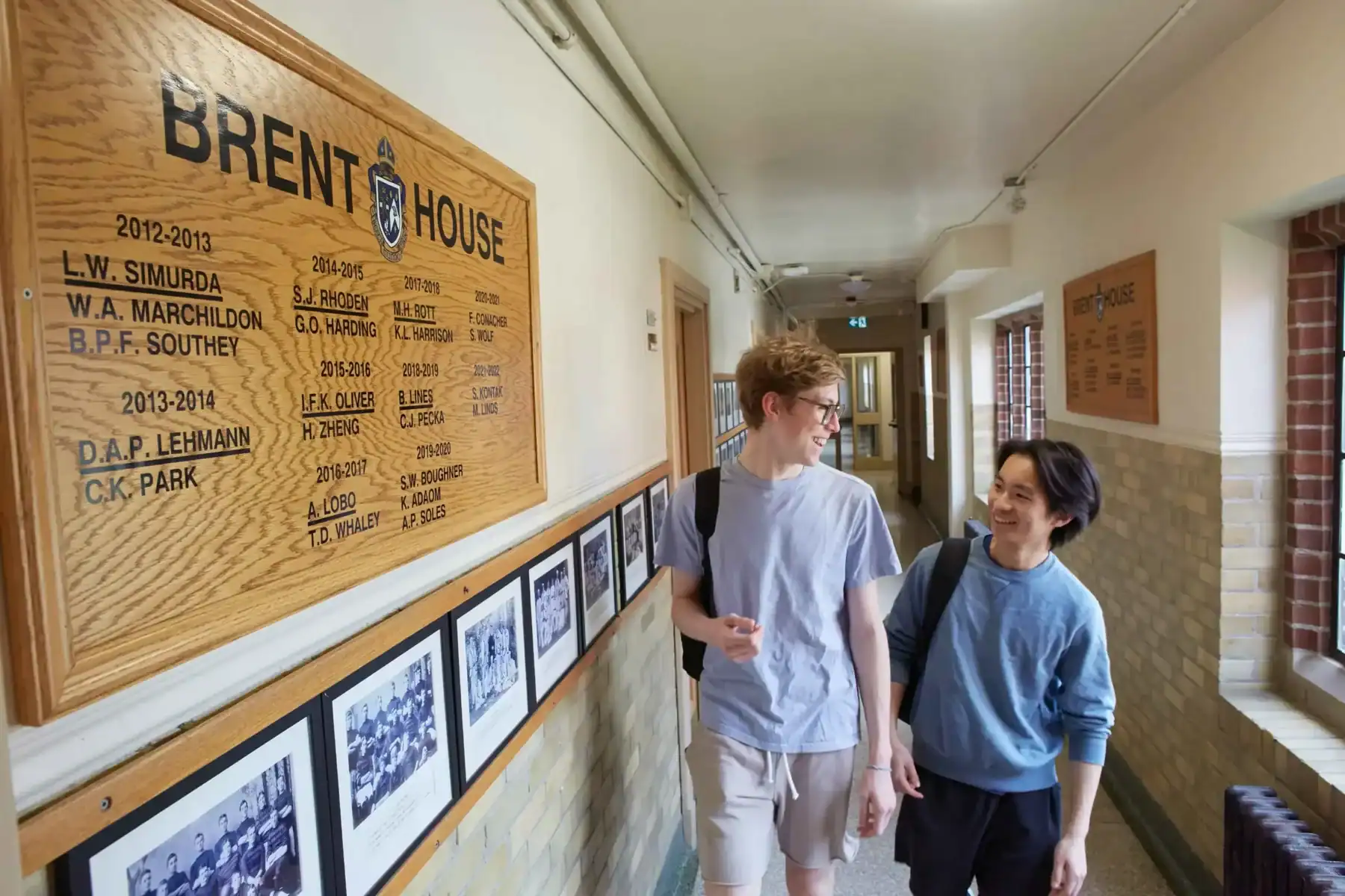 Students walking in a school corridor with historical plaques and photos on the wall.