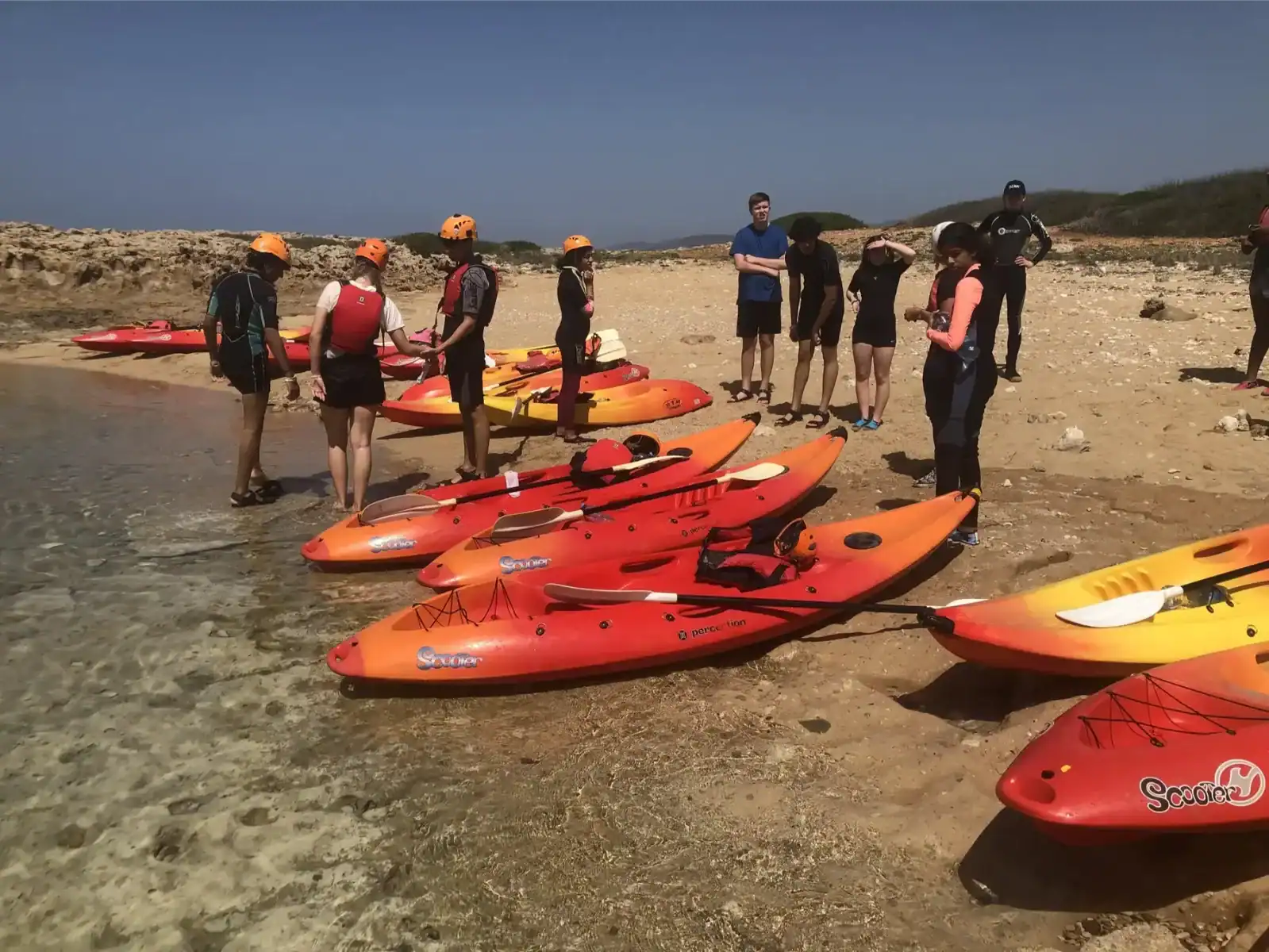 Kayakers preparing for a guided water adventure on a sandy beach. Group learning kayaking skills wit.