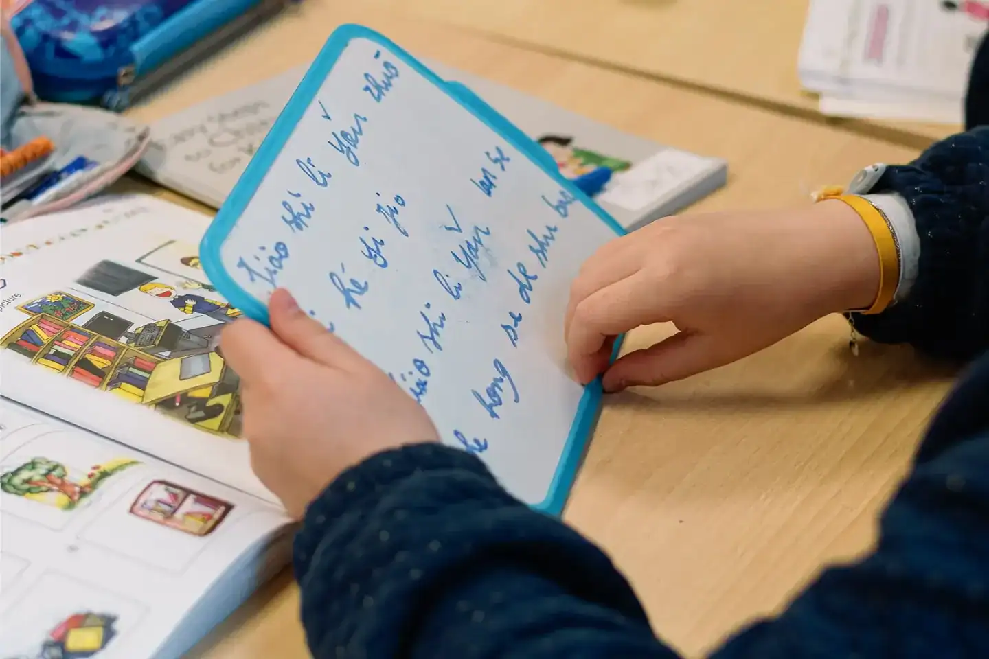 Child writing on a small whiteboard with a blue border in a classroom setting.