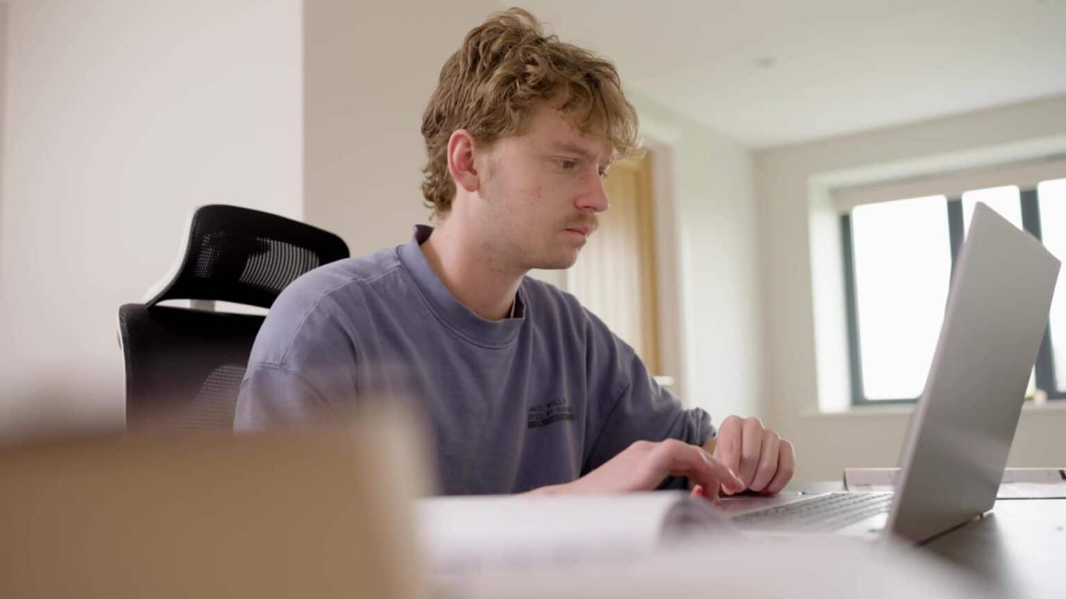 Student studying on a laptop in a bright, modern classroom setting.