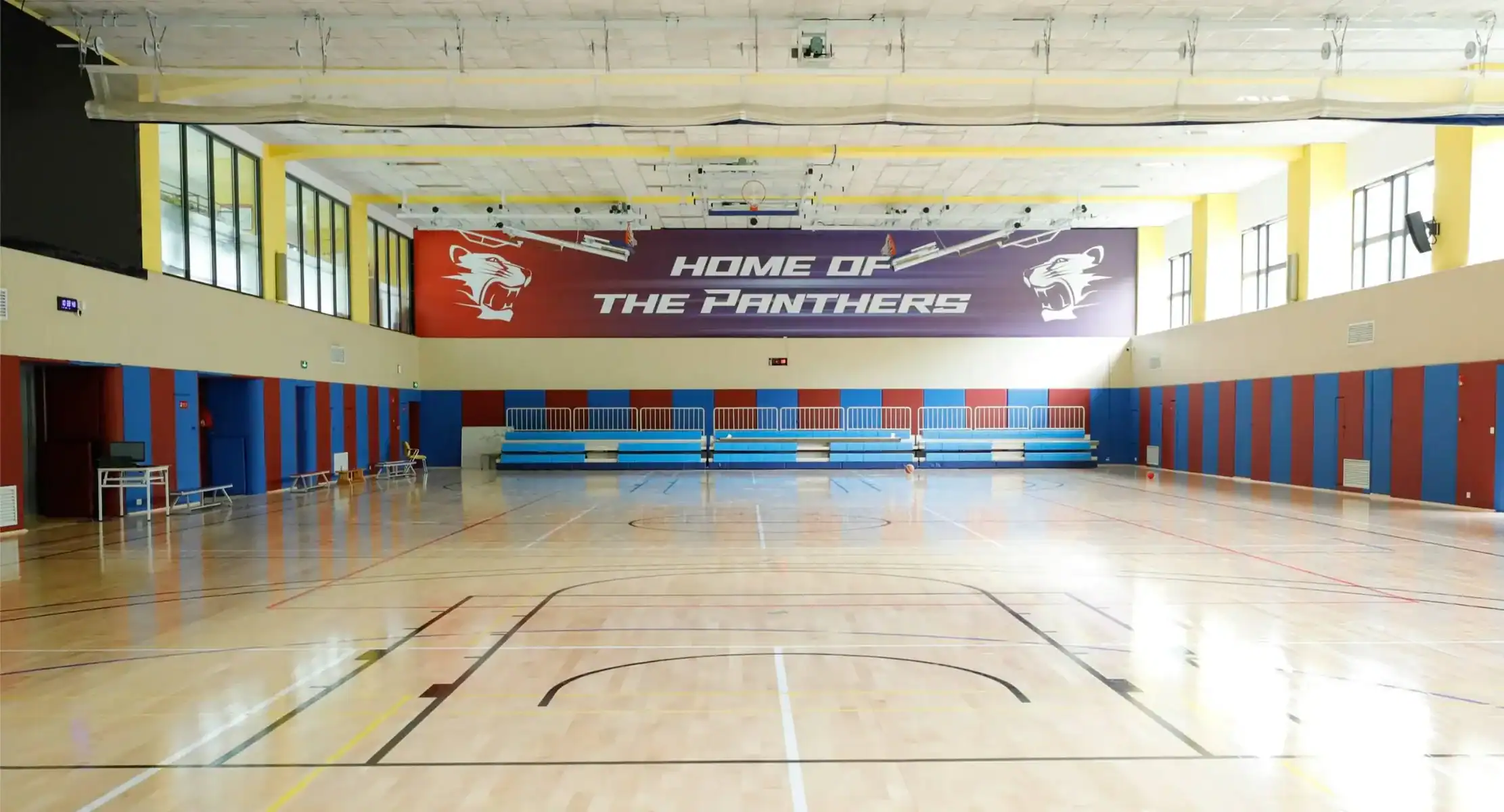 Indoor sports hall at Dulwich College Shanghai Pudong, featuring a basketball court and vibrant scho.