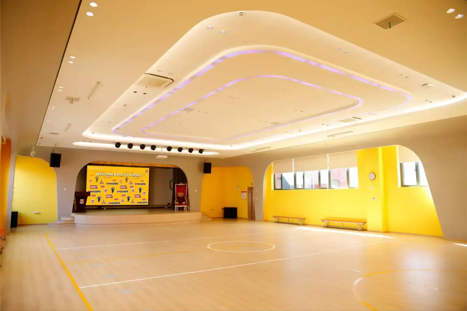 Indoor sports hall with bright yellow walls and a polished wooden floor at Dulwich College Shanghai.