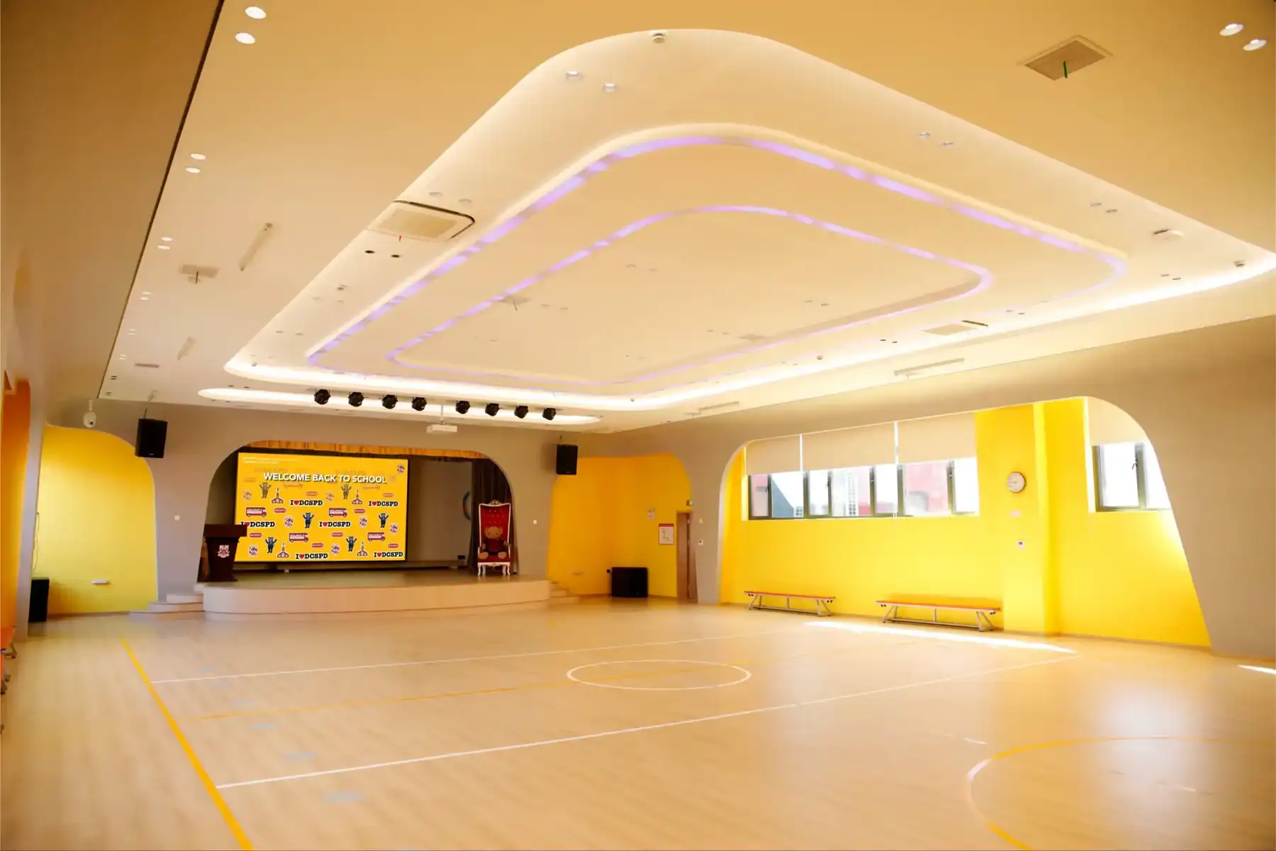 Indoor sports hall with bright yellow walls and a polished wooden floor at Dulwich College Shanghai.