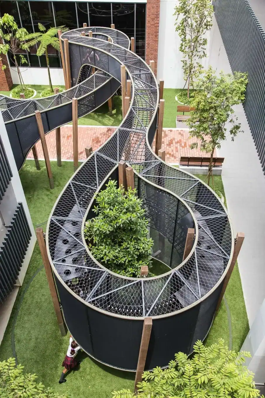 Outdoor school playground with winding elevated walkway and greenery.