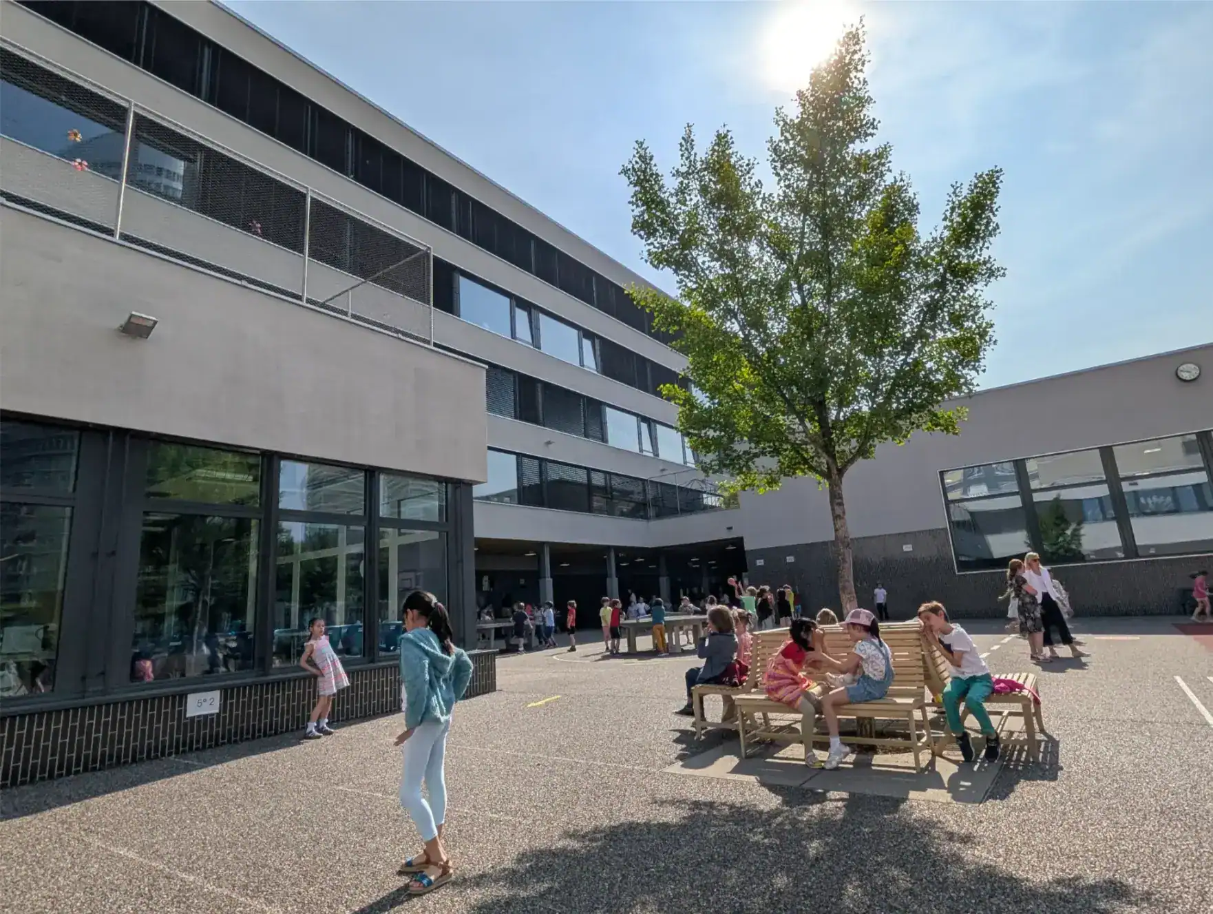 Modern international school building with students playing and socializing outdoors on a sunny day.