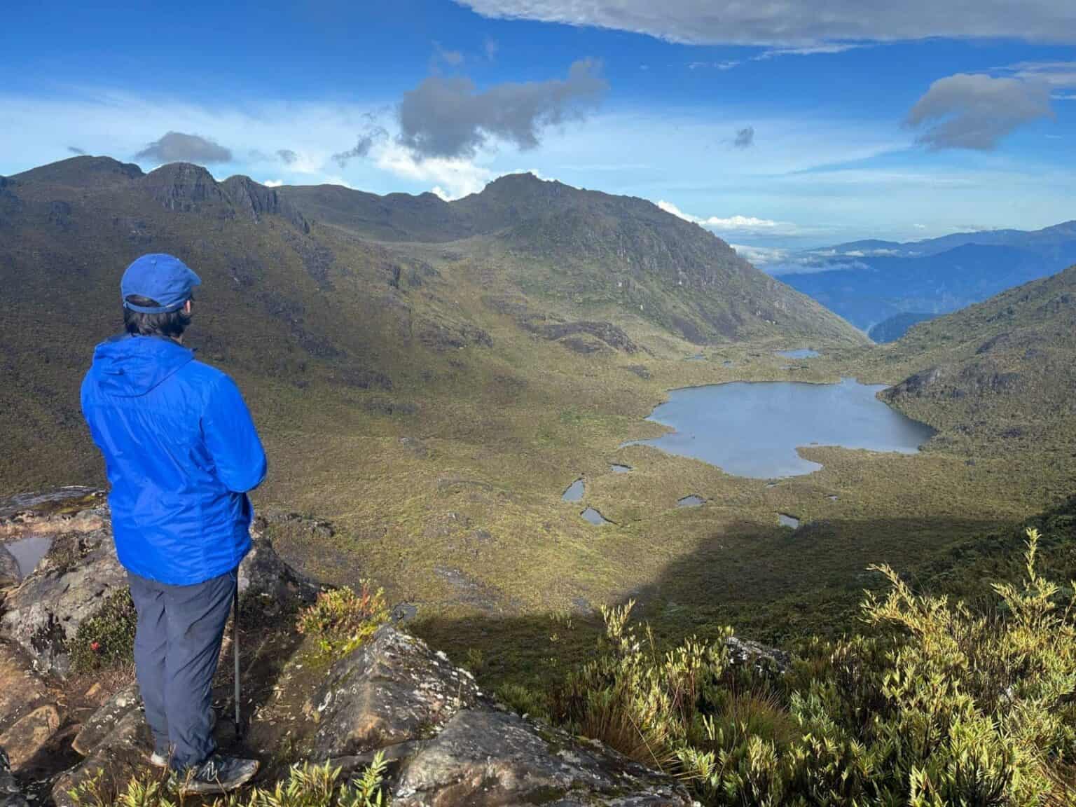 Scenic mountain landscape with a person in blue jacket overlooking valleys and lakes.