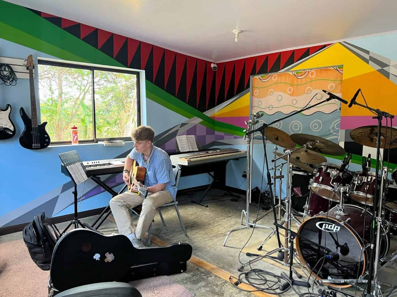Colorful music room with student practicing guitar, musical instruments, and vibrant wall art at an international school.