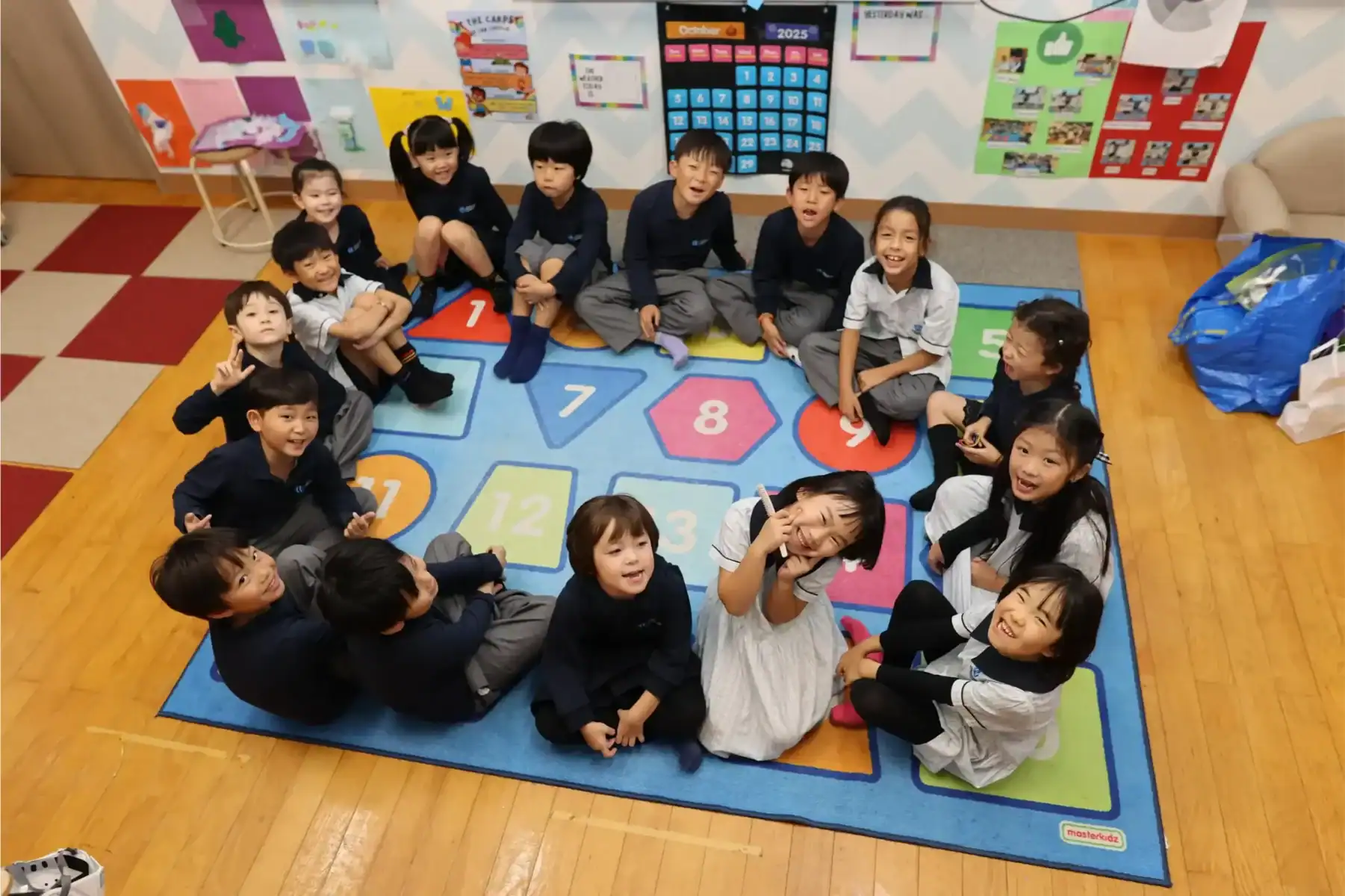 Bright young students sitting in a circle on a colorful educational carpet at a world school classroom.