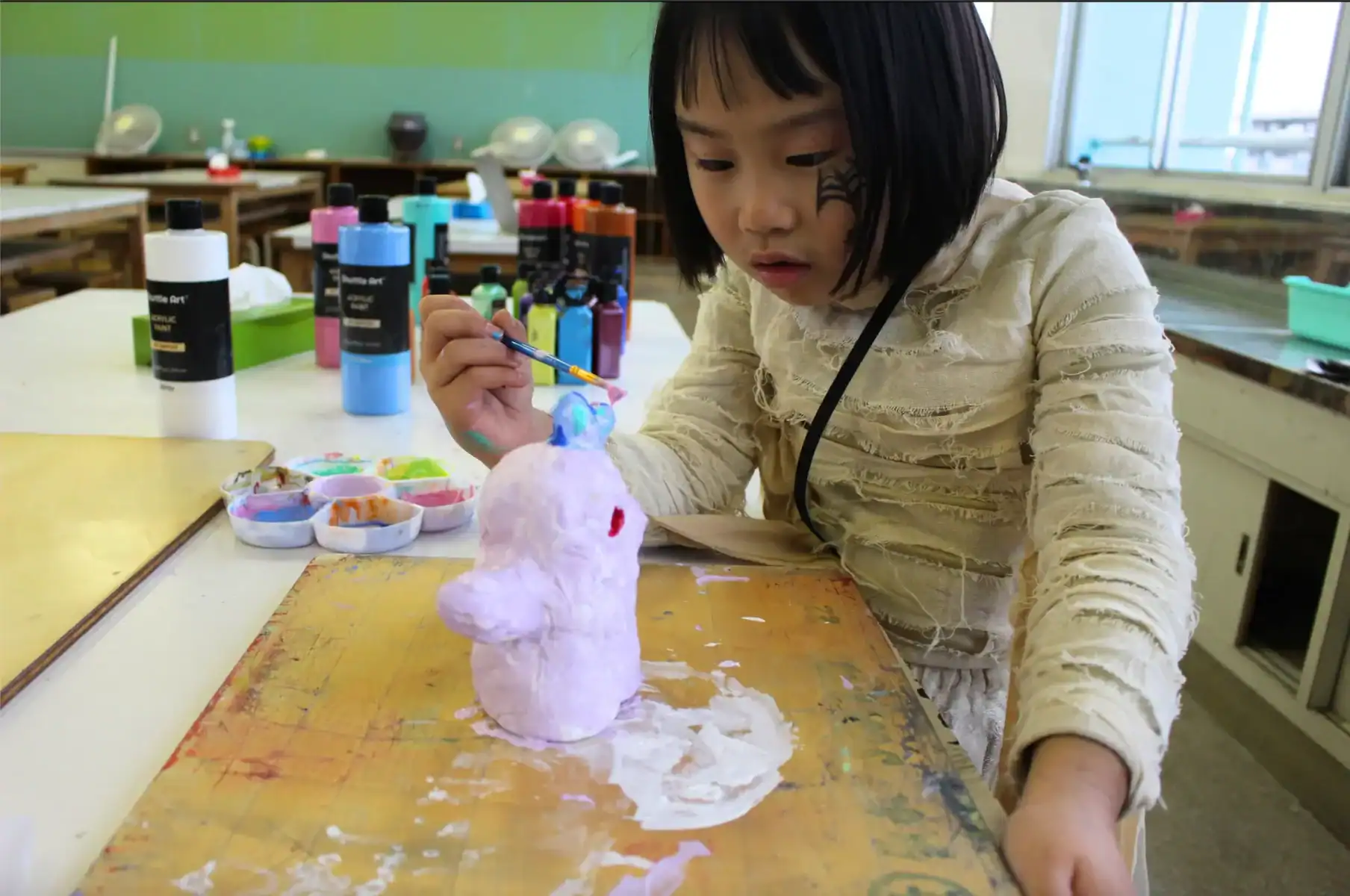Colorful art student painting a ceramic sculpture in classroom environment.