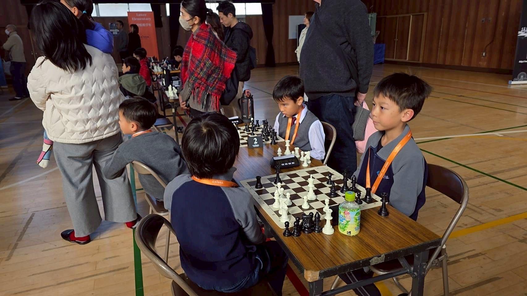 Young students playing chess at a school tournament in an indoor gymnasium.