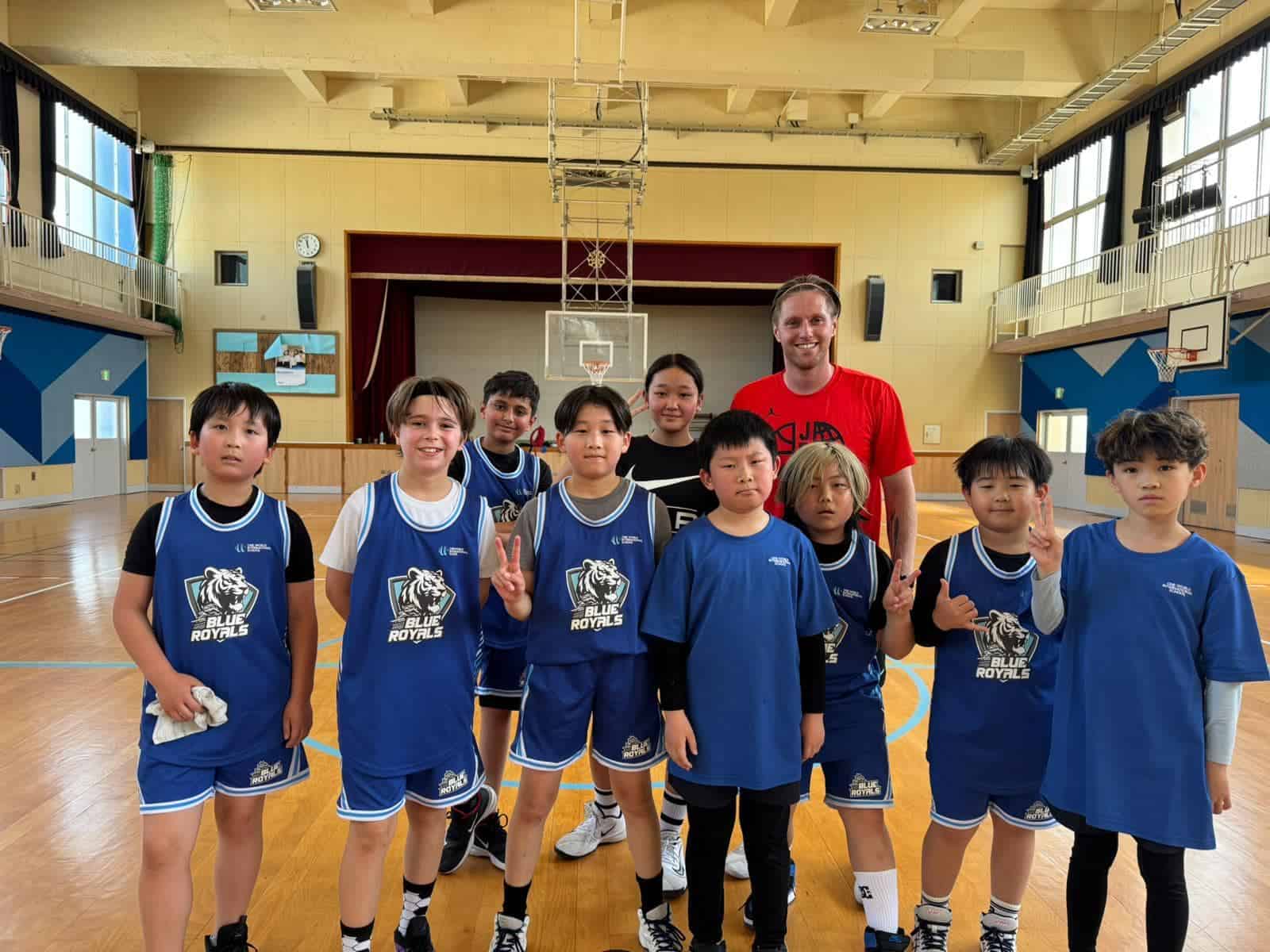 Young students in sports uniforms with a coach in a school gymnasium for basketball training and teamwork.