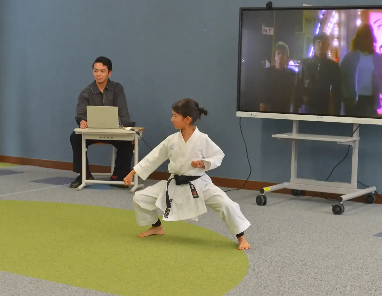 1. Young girl practicing karate in a classroom with a monitor in the background.