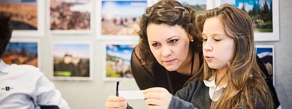 Focused teacher assisting young student with geography project at World Schools, promoting academic excellence.