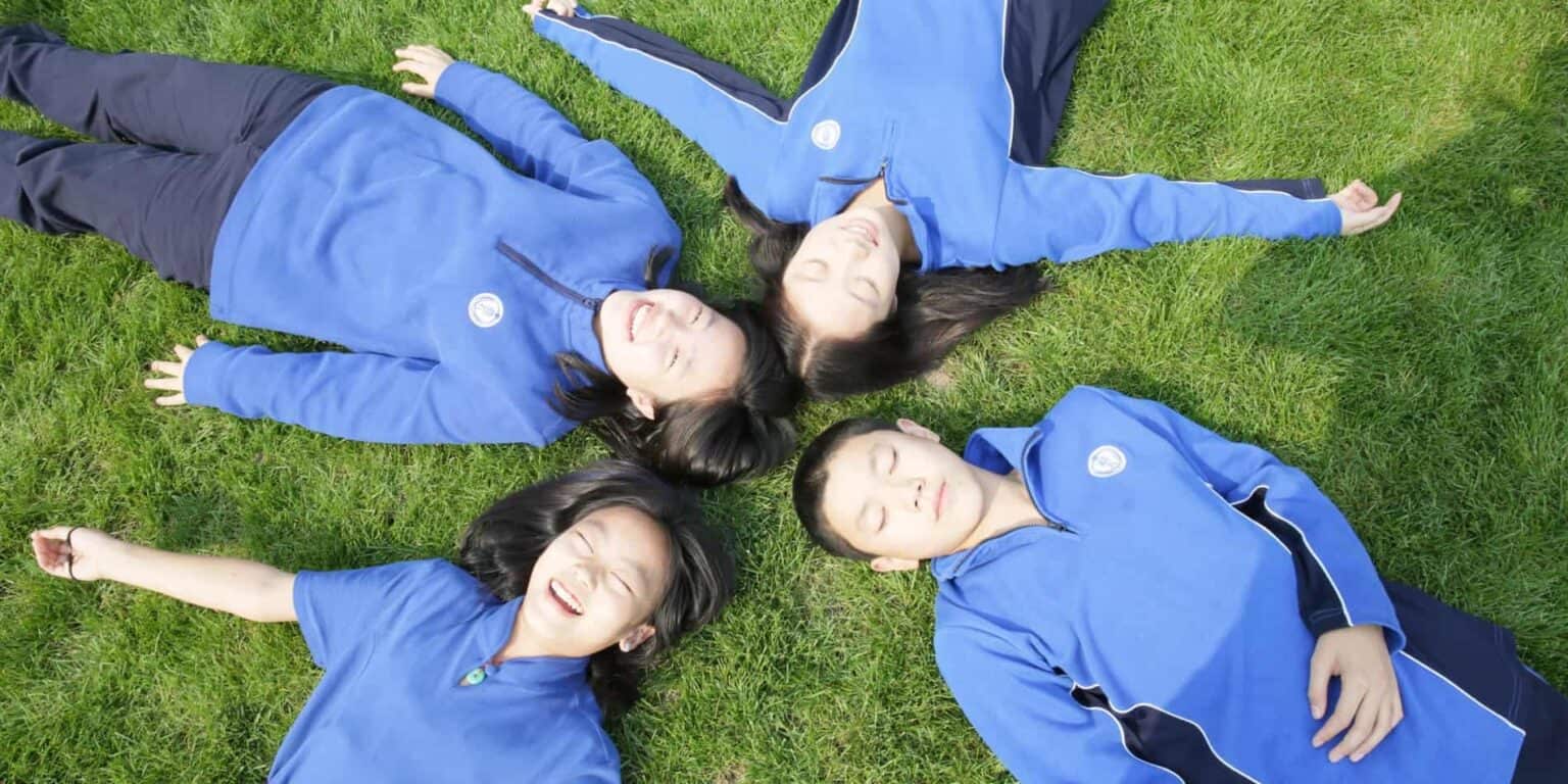 Lachende leerlingen liggen op het gras in schooluniformen, genietend van buitenonderwijs en vriendschap.