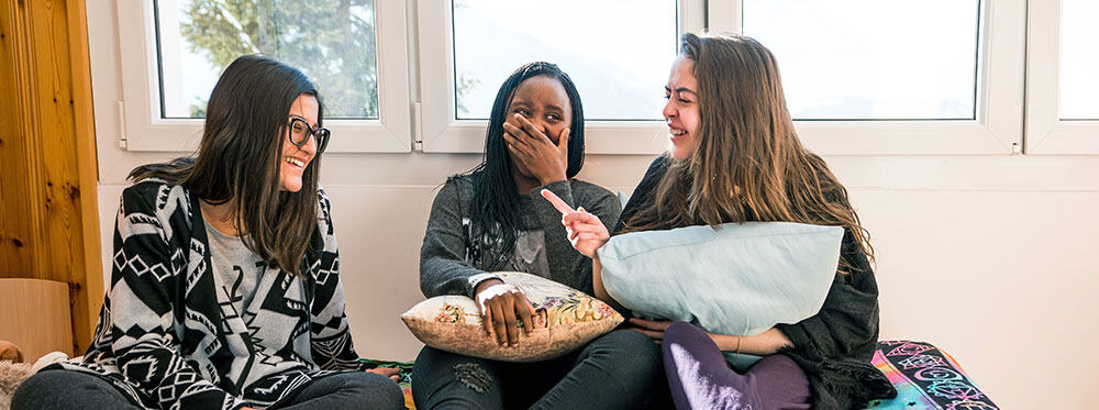 Friendly diverse schoolgirls laughing and chatting in classroom, positive learning environment, student friendship, multicultural education, World Schools.