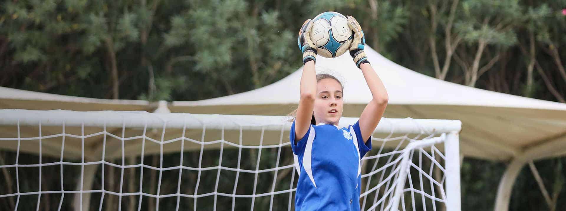 Youth girl goalkeeper catching soccer ball during practice on field.