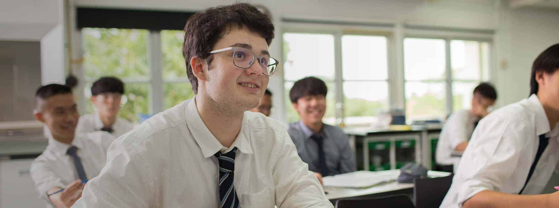 Bright Asian male student in classroom smiling with classmates during school lesson.