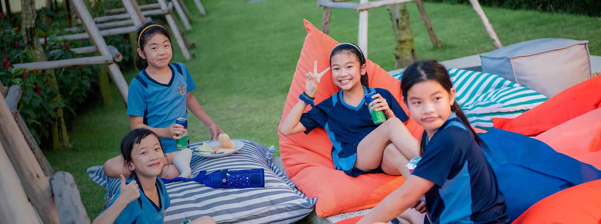 Happy schoolchildren enjoying outdoor activity, picnic, and play at a green garden setting.