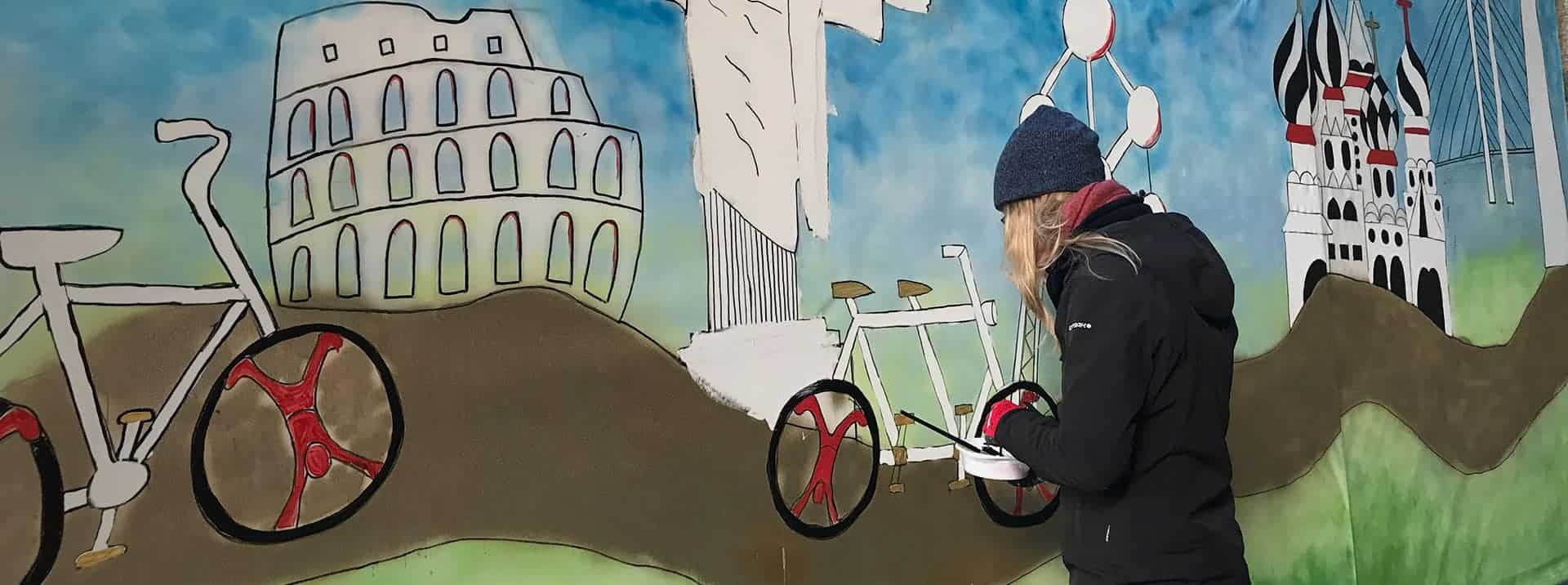 Colorful mural of famous landmarks with a person painting, representing world culture and education.