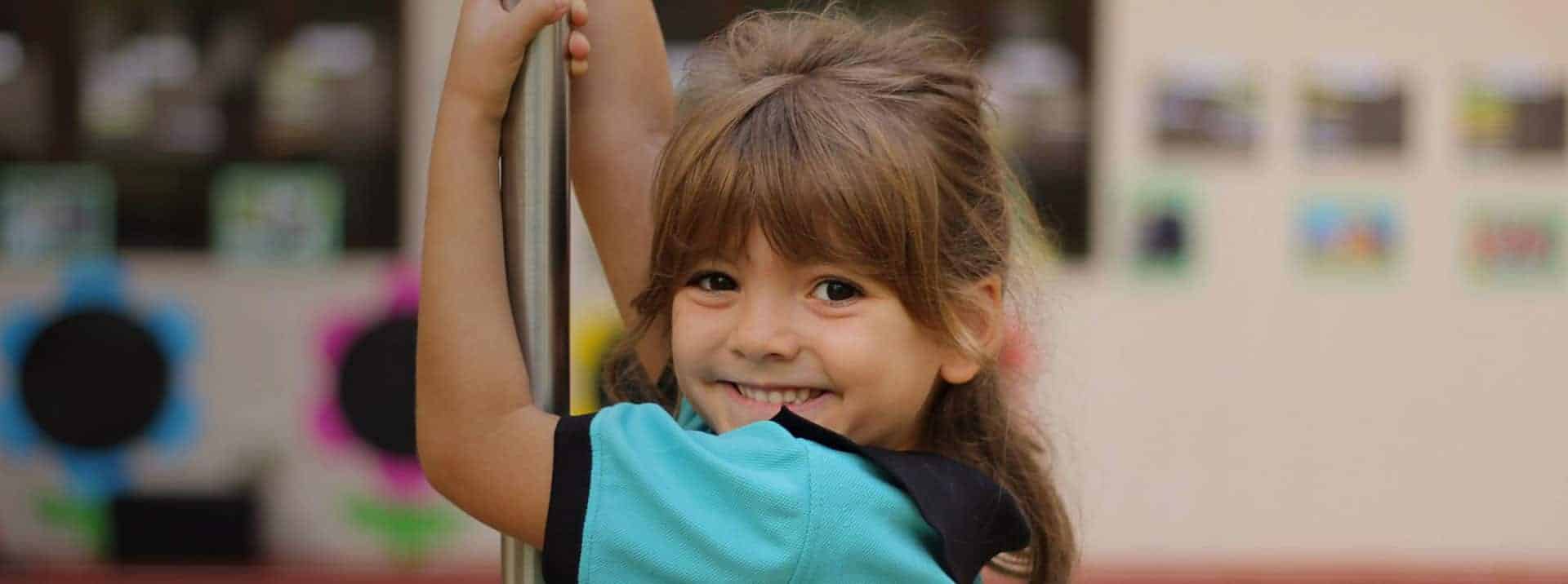 Bright smiling girl holding playground equipment at international school playground.